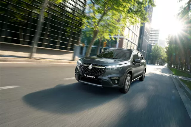 Side view of a grey Suzuki S-Cross on an asphalt road at sunset.