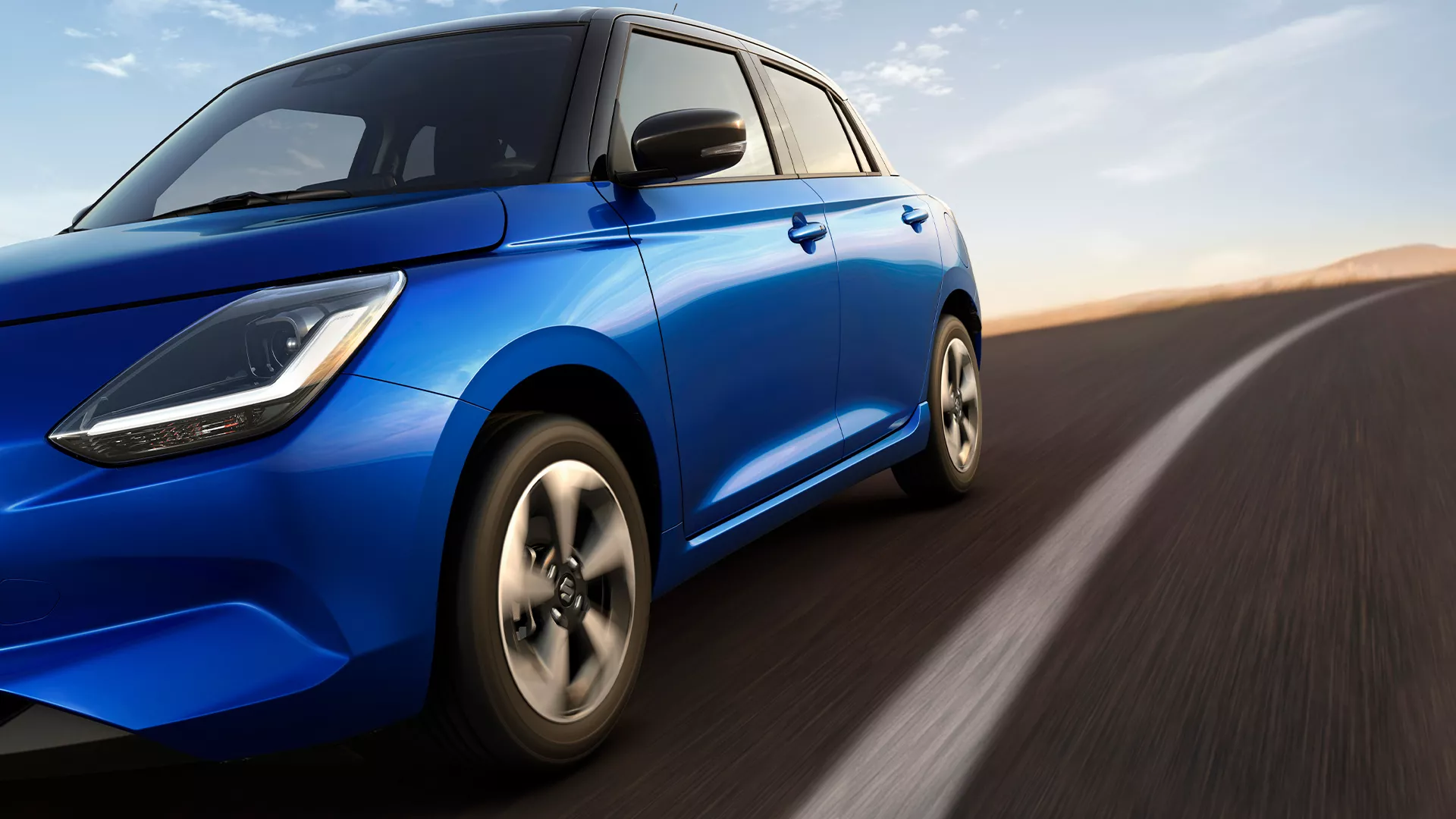 Dynamic front-side view of the Suzuki Swift AllGrip 4-wheel drive in motion on an open road, showcasing its performance and control.