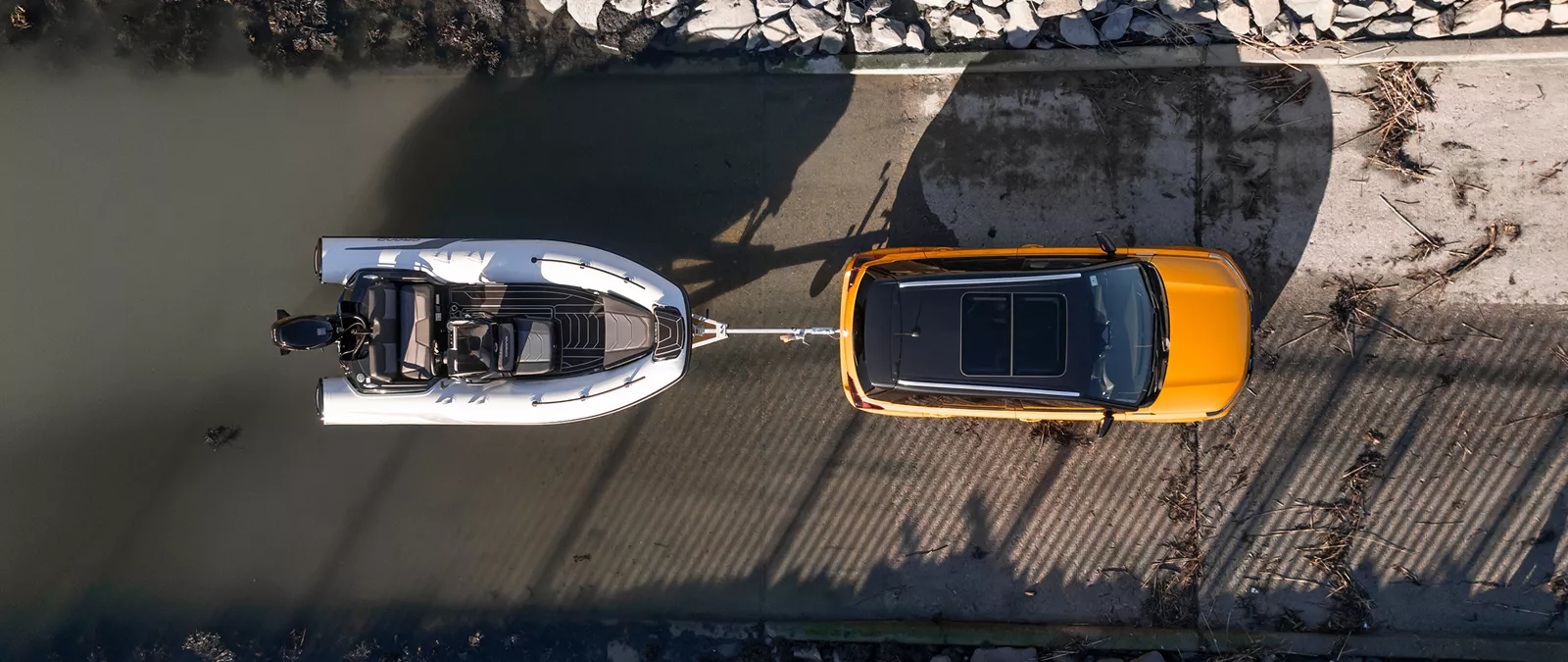 Birds eye view of an solar yellow Suzuki Vitara towing a boat down a slipway into the water, demonstrating its towing capability.