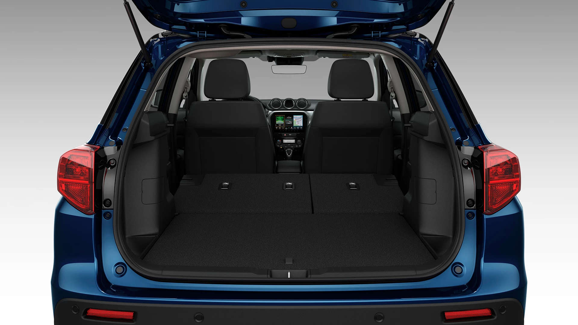 Rear view of the Suzuki Vitara with the tailgate open, showcasing the spacious boot area and flat-folding rear seats for expanded cargo capacity.