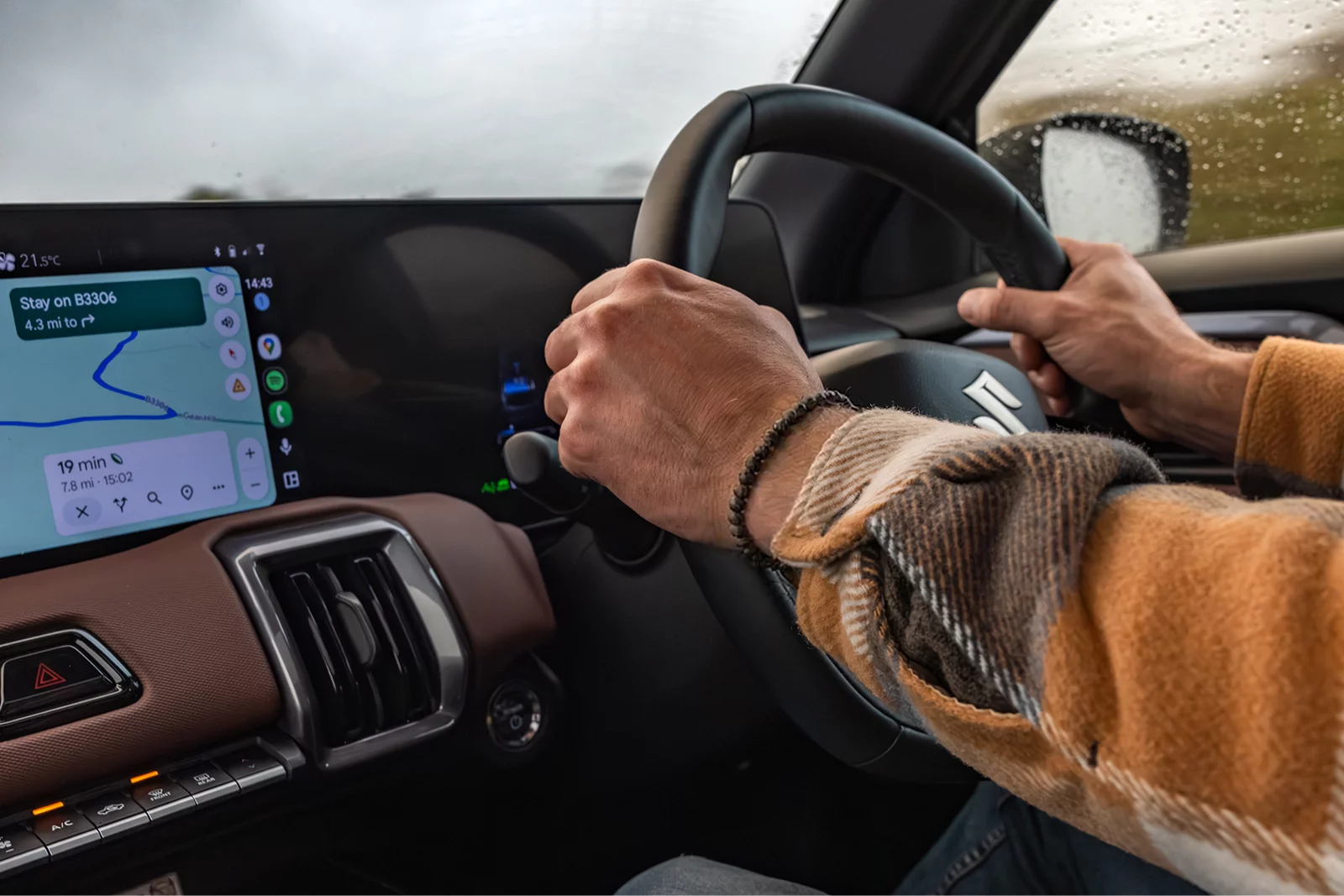 Driver holding the steering wheel inside a Suzuki vehicle with navigation displayed on the dashboard