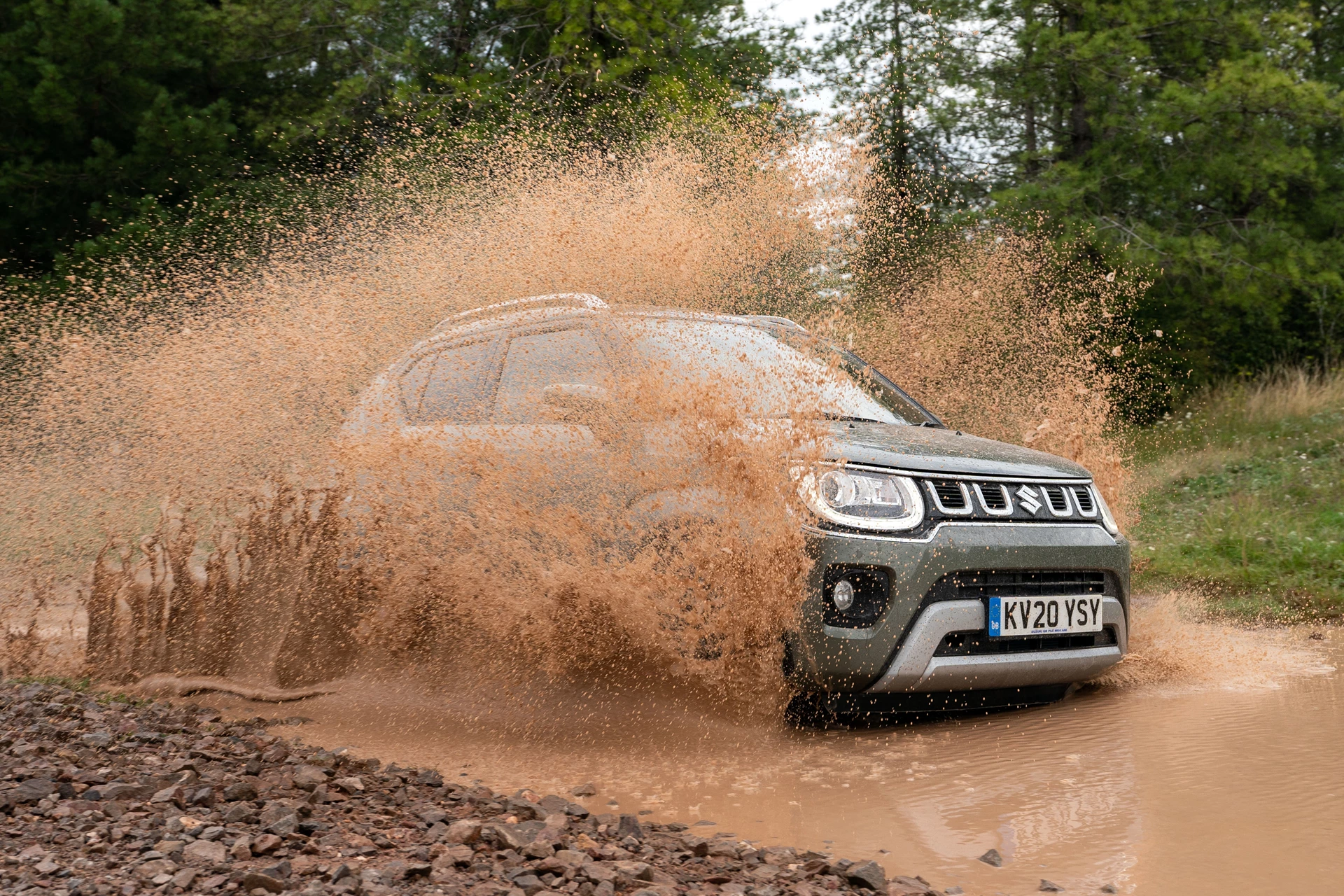 Suzuki Ignis moving through wet terrain surrounded by trees.