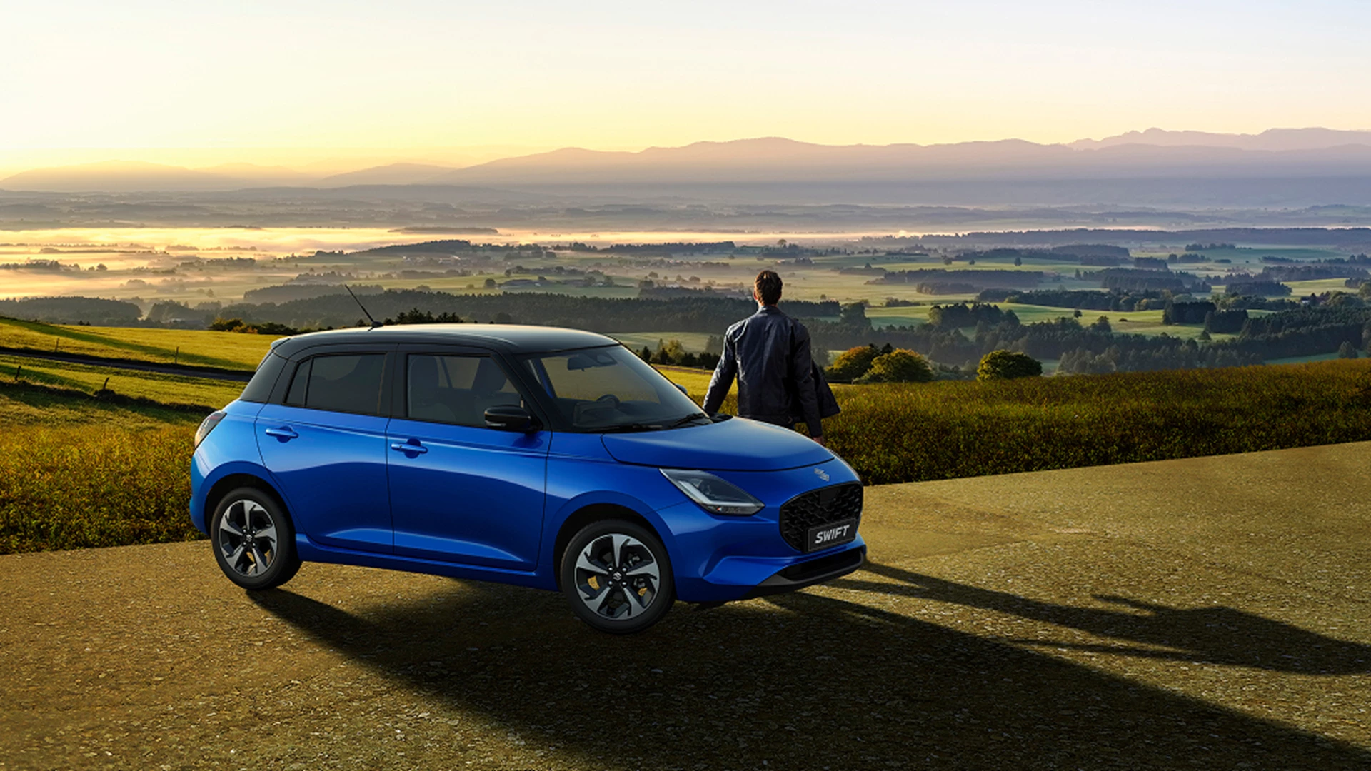 Suzuki Swift overlooking a misty mountain landscape at sunrise, looking out at the valley.