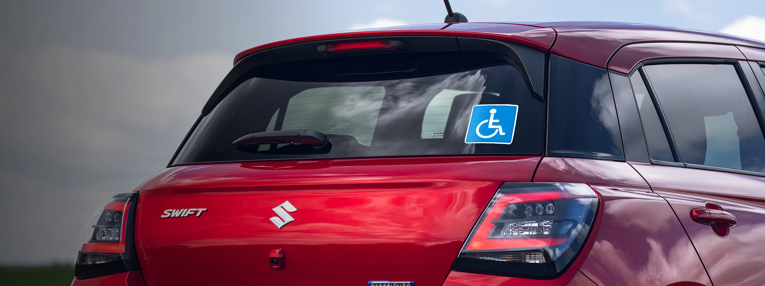 Rear view of a red Suzuki Swift with a Motability wheelchair accessibility sticker on the rear window
