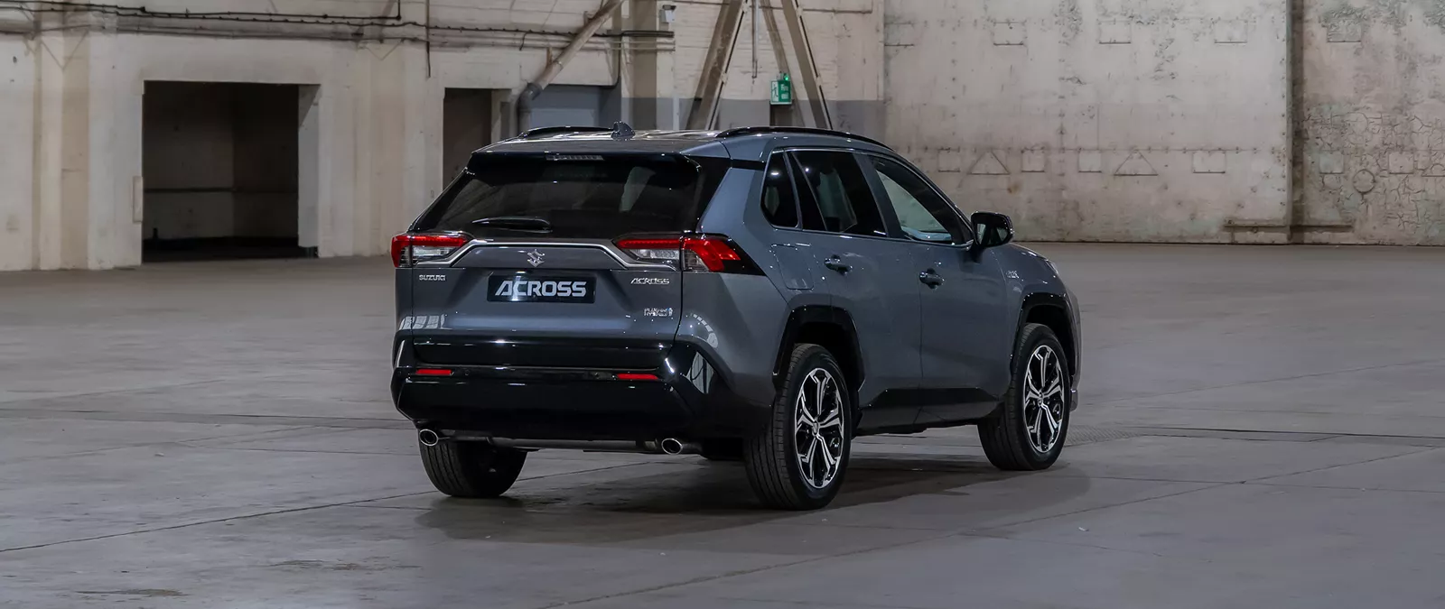 Rear view of a Suzuki Across SUV in a grey metallic finish, positioned in an industrial warehouse setting.