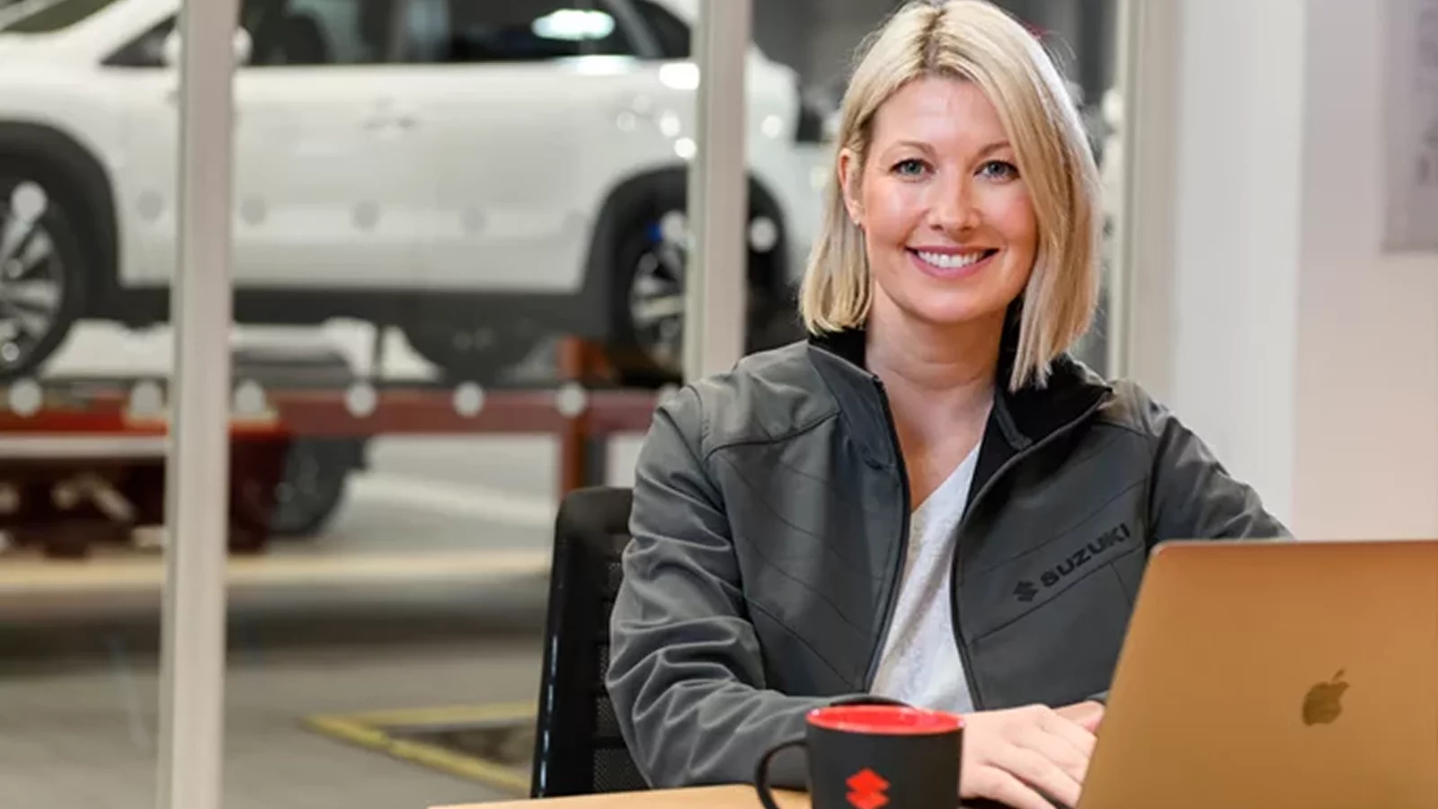 Suzuki employee sitting at a desk with a laptop inside a dealership showroom