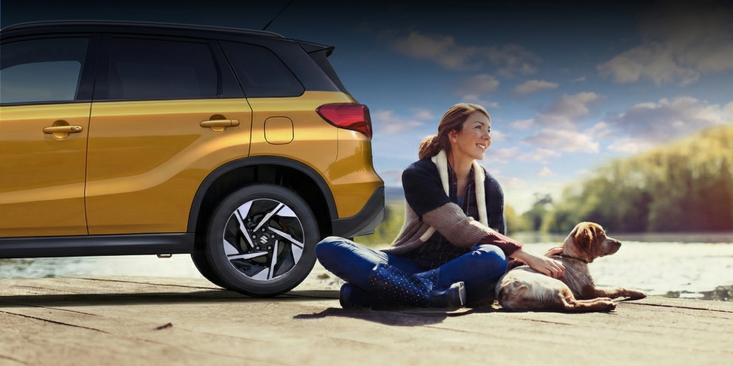 Woman sitting beside a yellow Suzuki SUV with a dog by the water