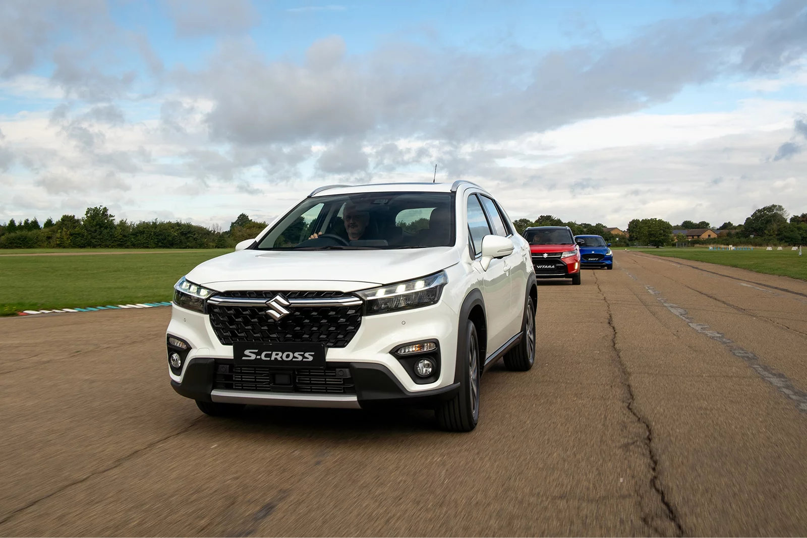 White Suzuki S-Cross driving on a test track with other Suzuki models behind