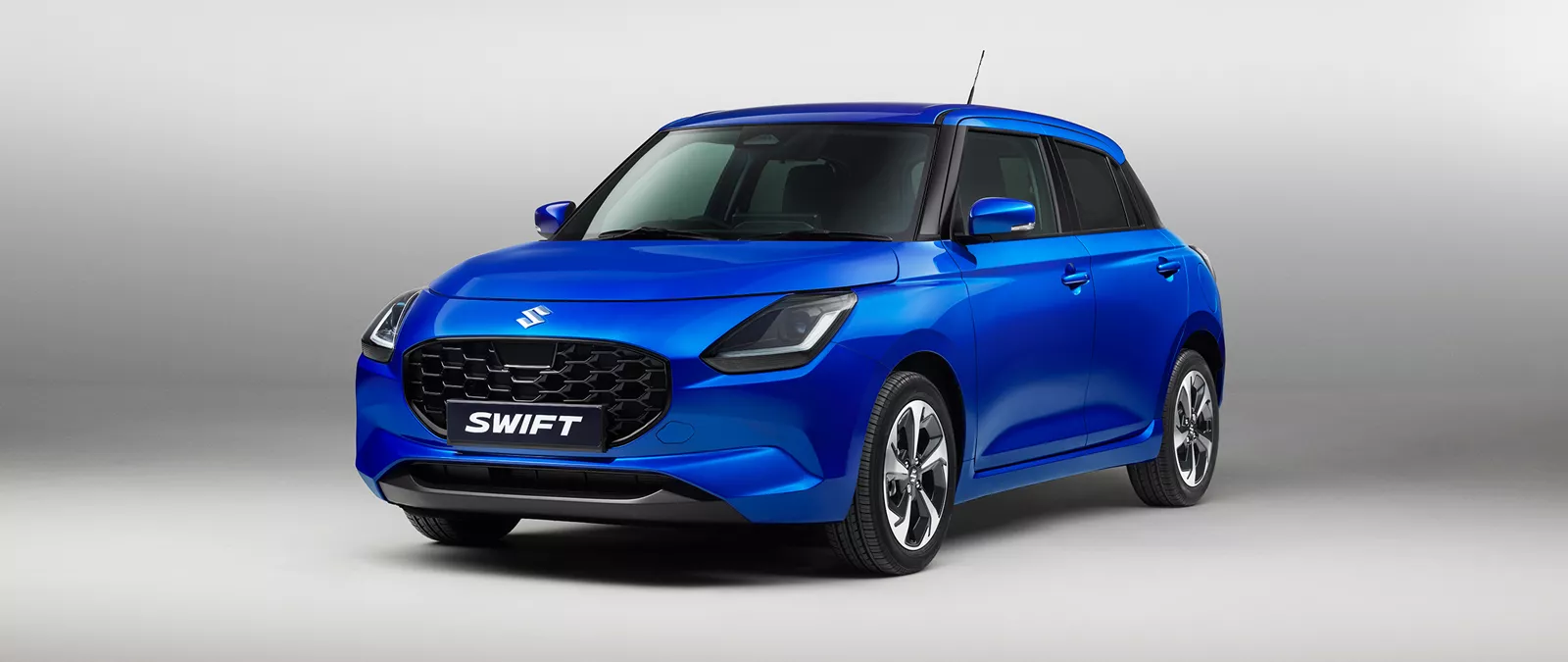 Front angle view of the Suzuki Swift in vibrant frontier blue pearl metallic, showcasing its bold grille and modern design