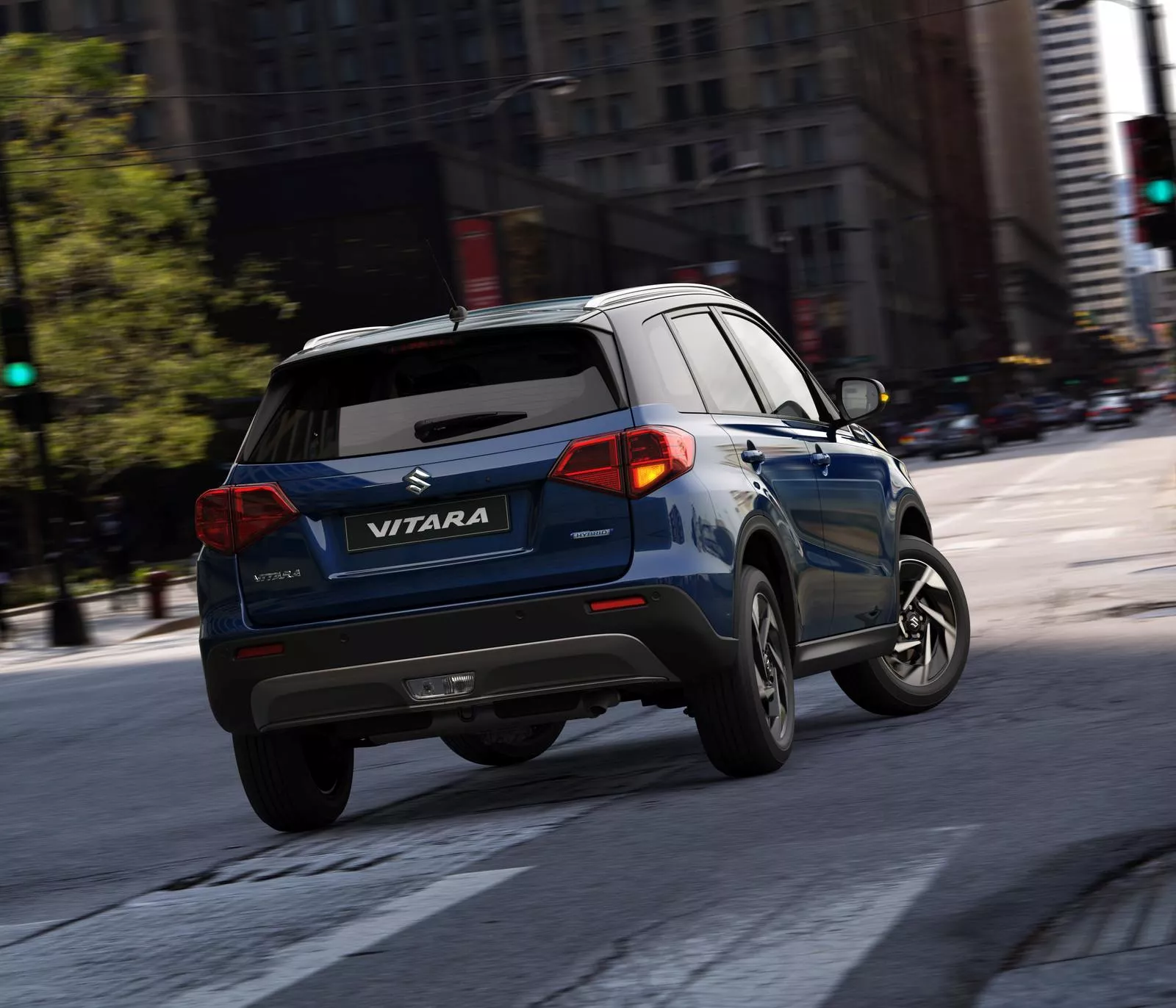 Rear view of the Suzuki Vitara in sphere blue driving through a city street, showcasing its urban styling and compact SUV design.
