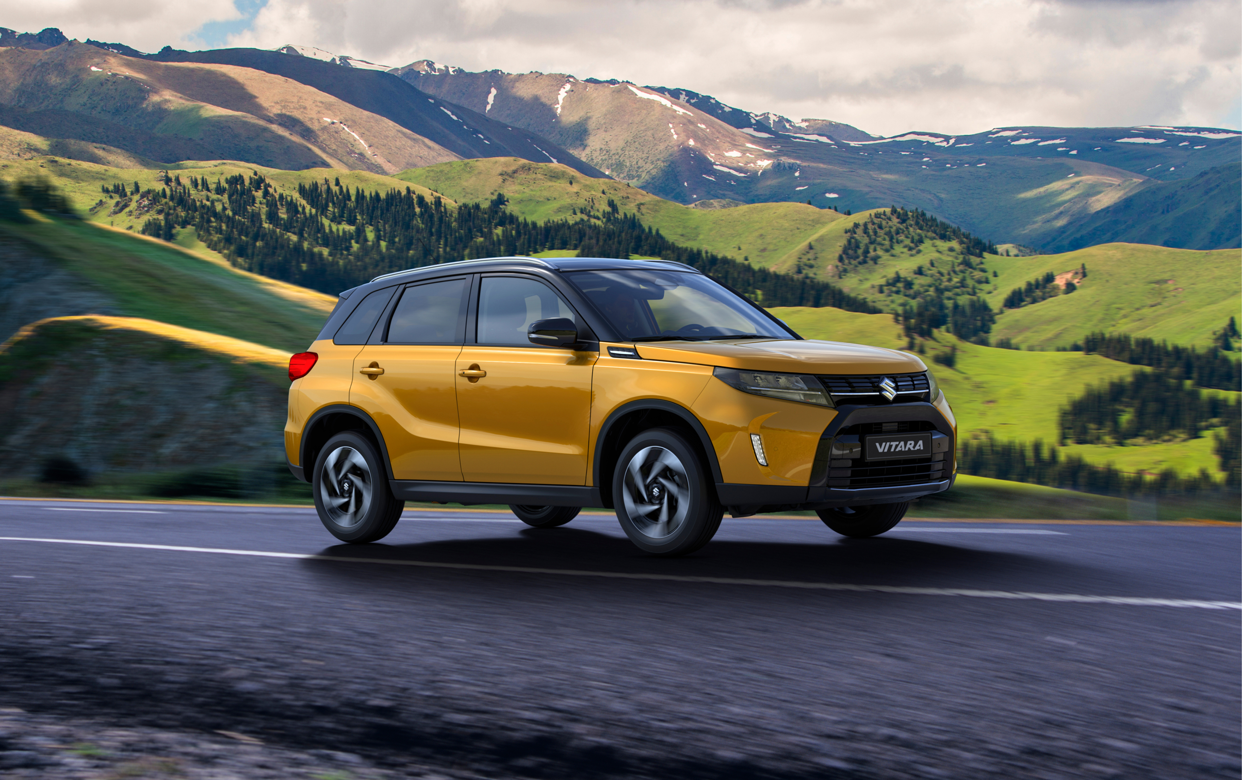 Side view of a Solar yellow Suzuki Vitara driving through a scenic mountain landscape, showcasing its bold design and all-terrain capability.
