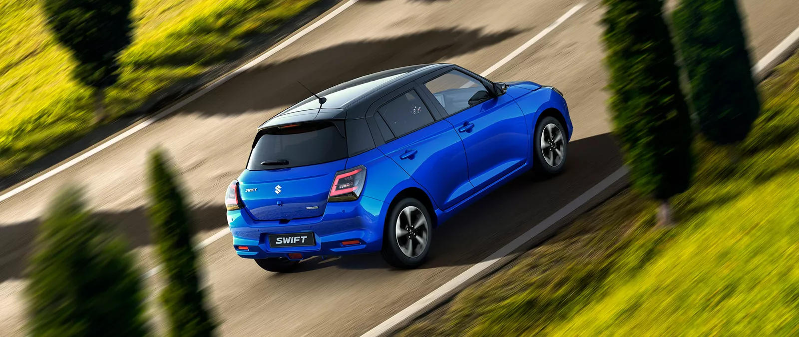 Rear and side view of the frontier blue Suzuki Swift driving on a winding road, highlighting its sporty design and dynamic performance.