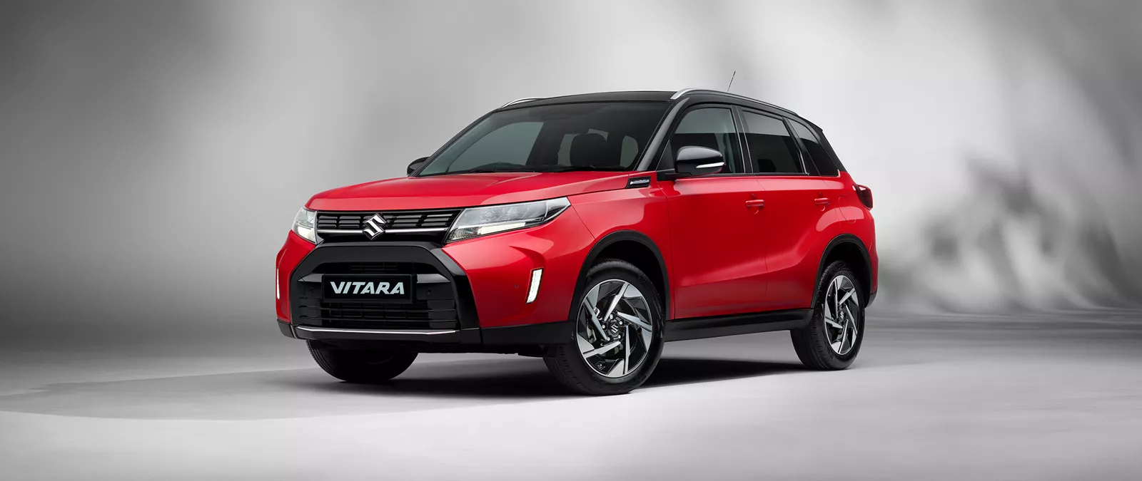 Front-side view of the Suzuki Vitara in dual tone bright red and cosmic black, displayed in a studio setting against a neutral grey background.