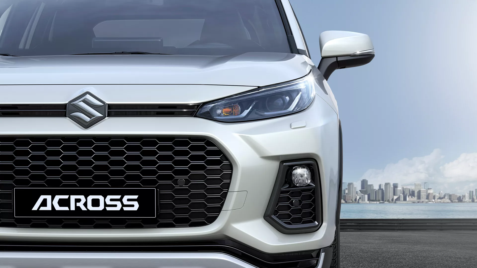 Front view of Suzuki Across highlighting its distinctive honeycomb grille, LED headlights, and bold SUV styling with city skyline backdrop