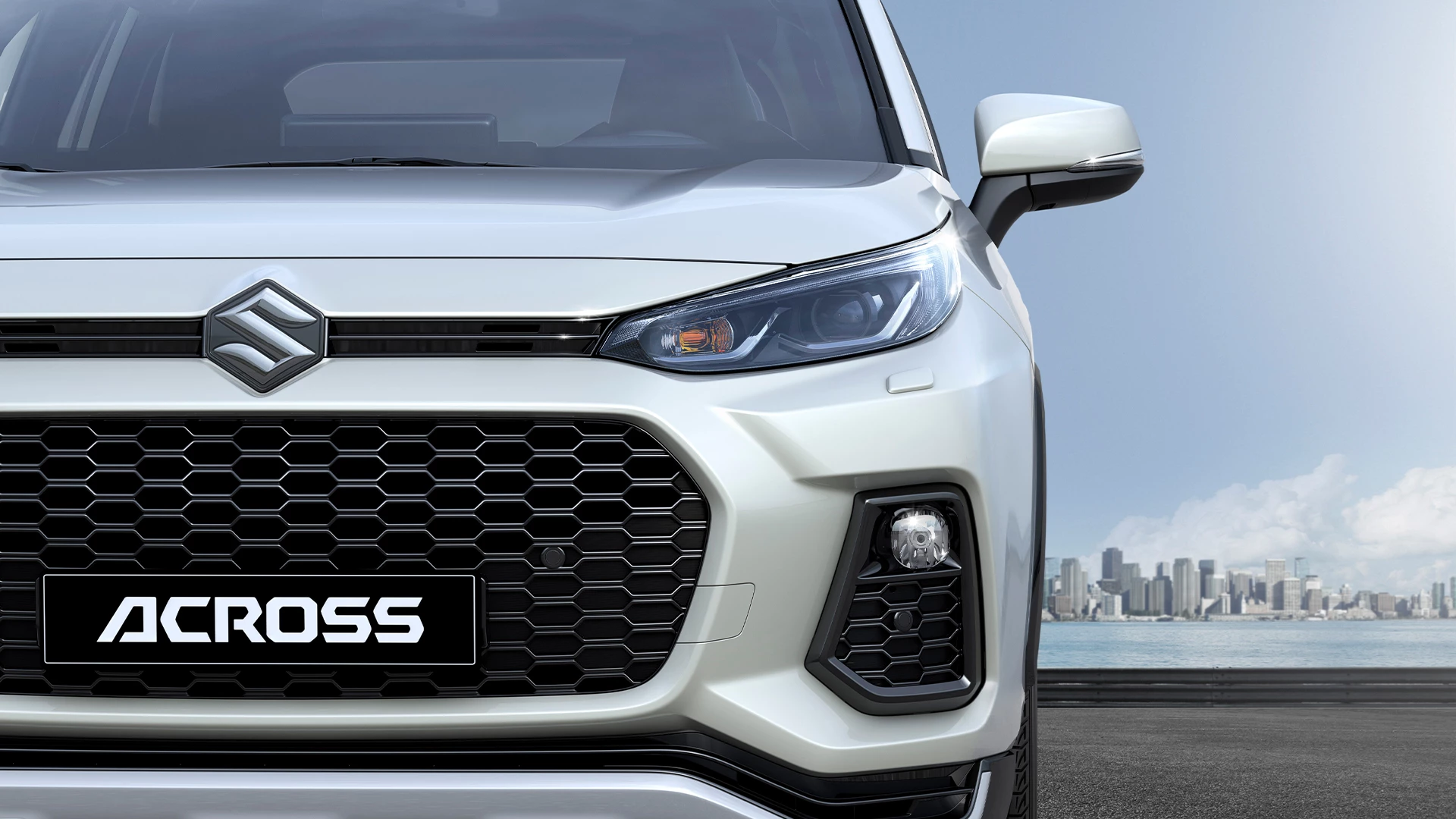 Front view of Suzuki Across highlighting its distinctive honeycomb grille, LED headlights, and bold SUV styling with city skyline backdrop