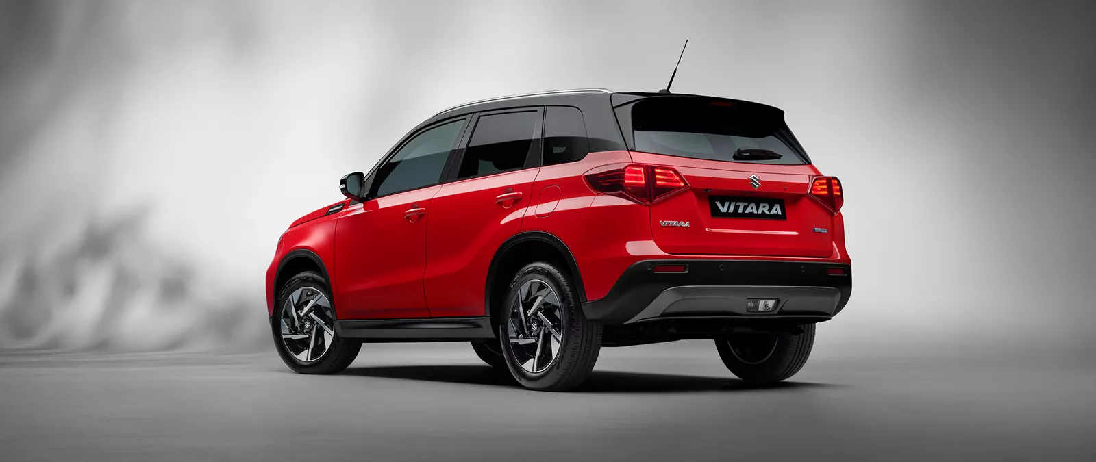 Rear view of the Suzuki Vitara in dual tone bright red and cosmic black, displayed in a studio setting against a neutral grey background.