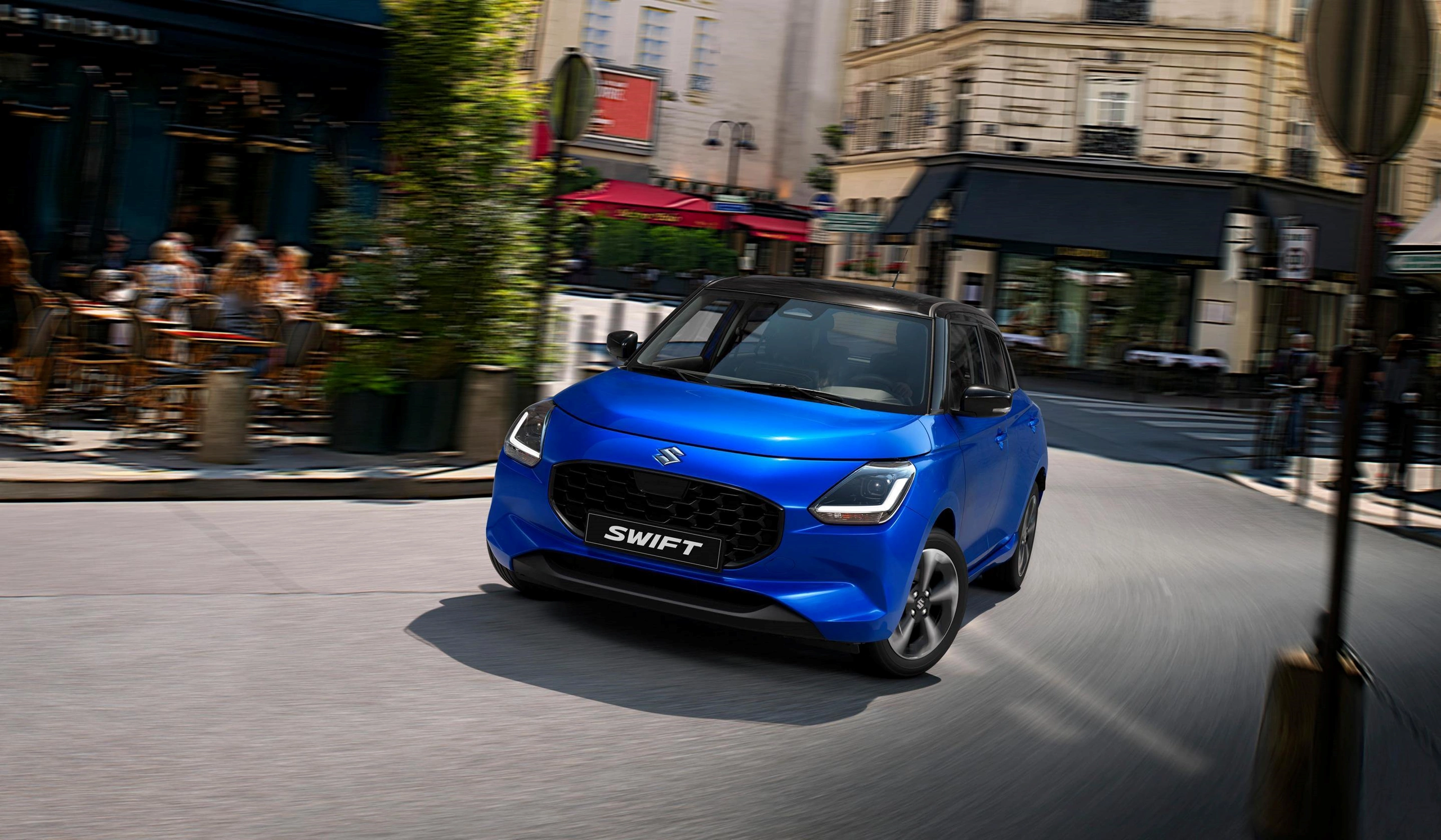 Suzuki Swift driving through a vibrant city street, showcasing its modern design.