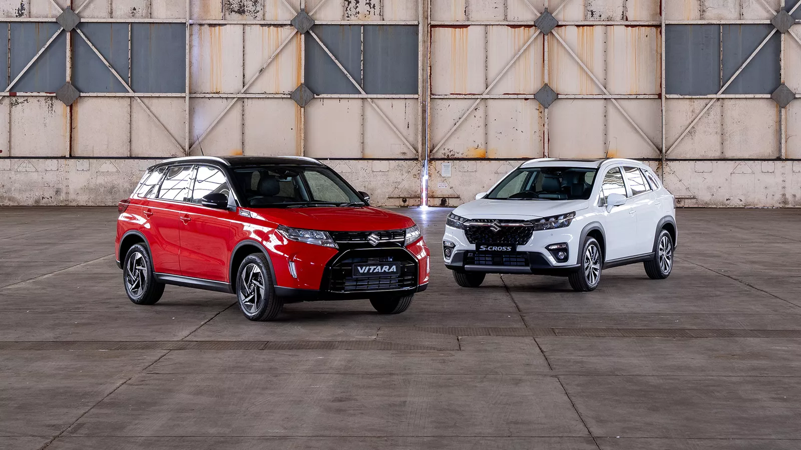 Red Suzuki Vitara and white Suzuki S-Cross parked inside an industrial warehouse
