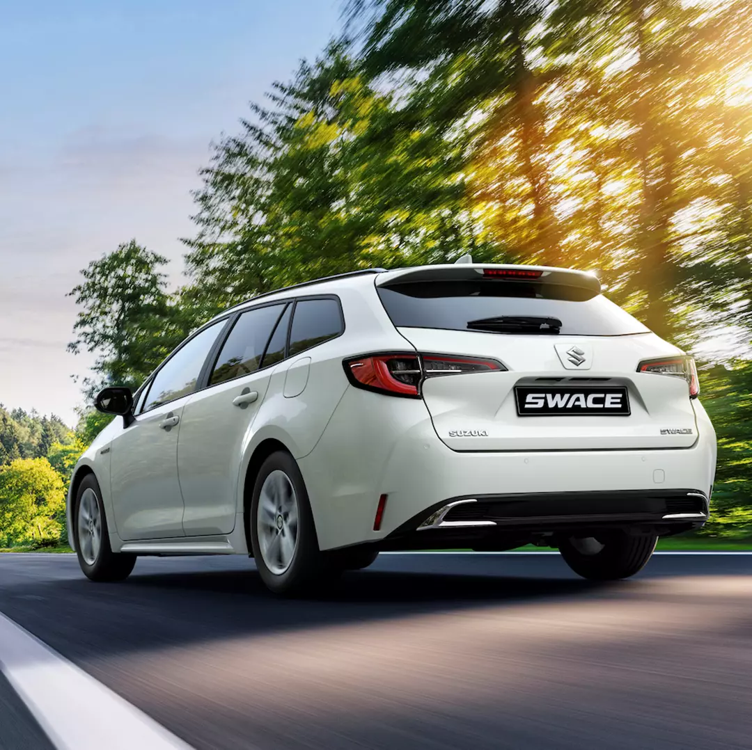 Rear view of a Platinum white Suzuki Swace driving through a beautiful countryside