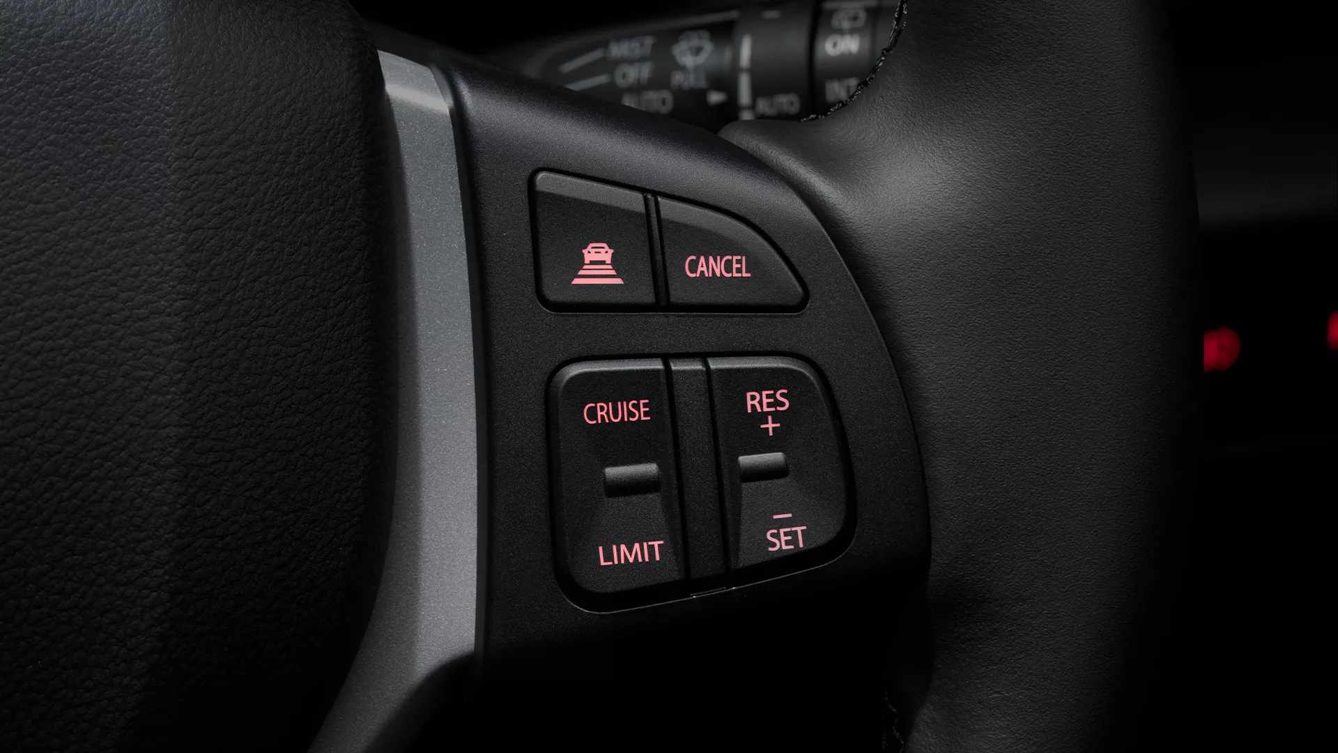 Close-up of the Suzuki S-Cross steering wheel controls, highlighting buttons for Adaptive Cruise Control, speed limiter, and cruise settings with illuminated icons.