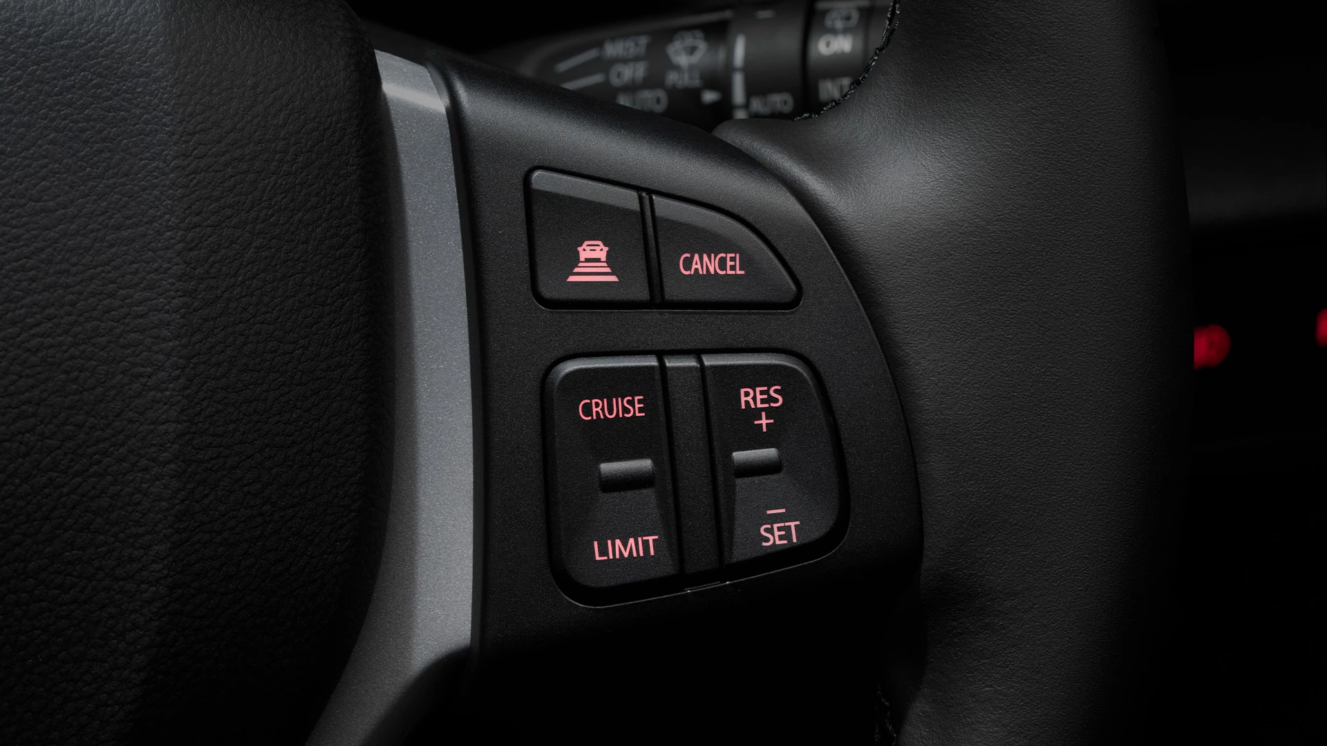 Close-up of the Suzuki S-Cross steering wheel controls, highlighting buttons for Adaptive Cruise Control, speed limiter, and cruise settings with illuminated icons.