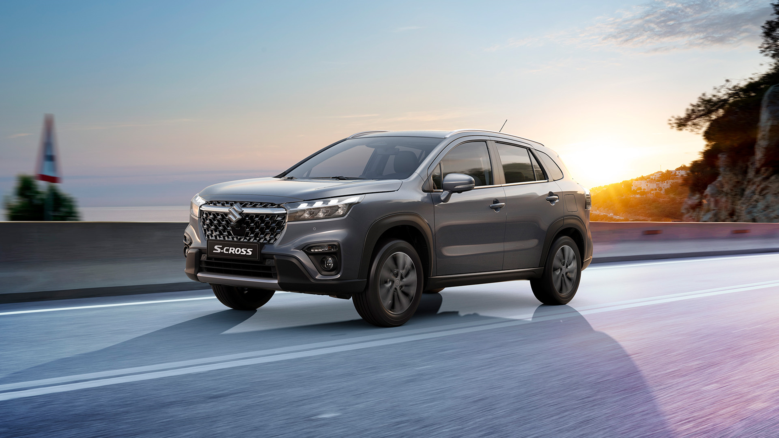 Suzuki S-Cross driving on coastal road at sunset, showcasing bold front grille and modern SUV styling.