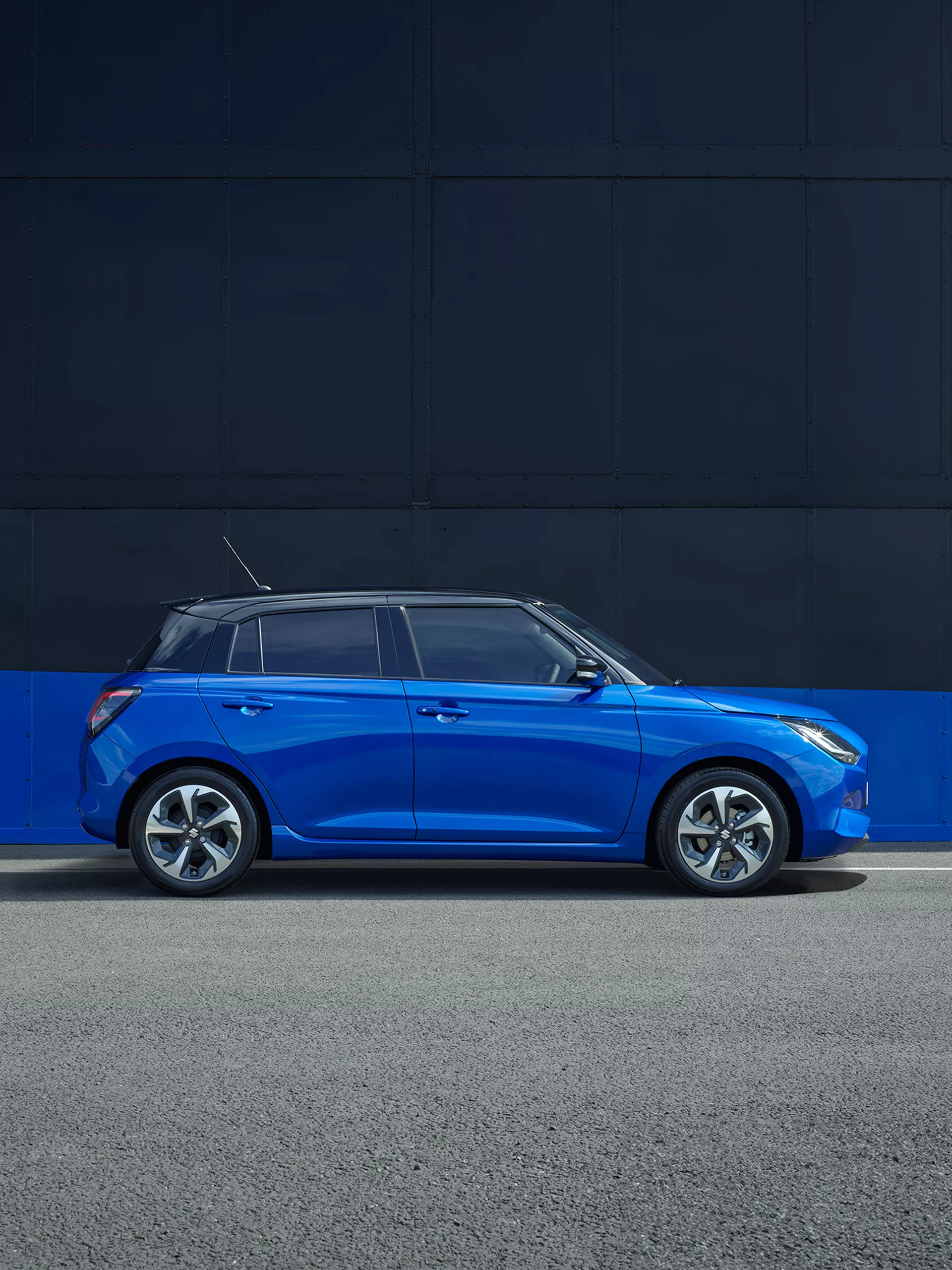 Side view of the Suzuki Swift Hybrid parked in frontier blue and super black.