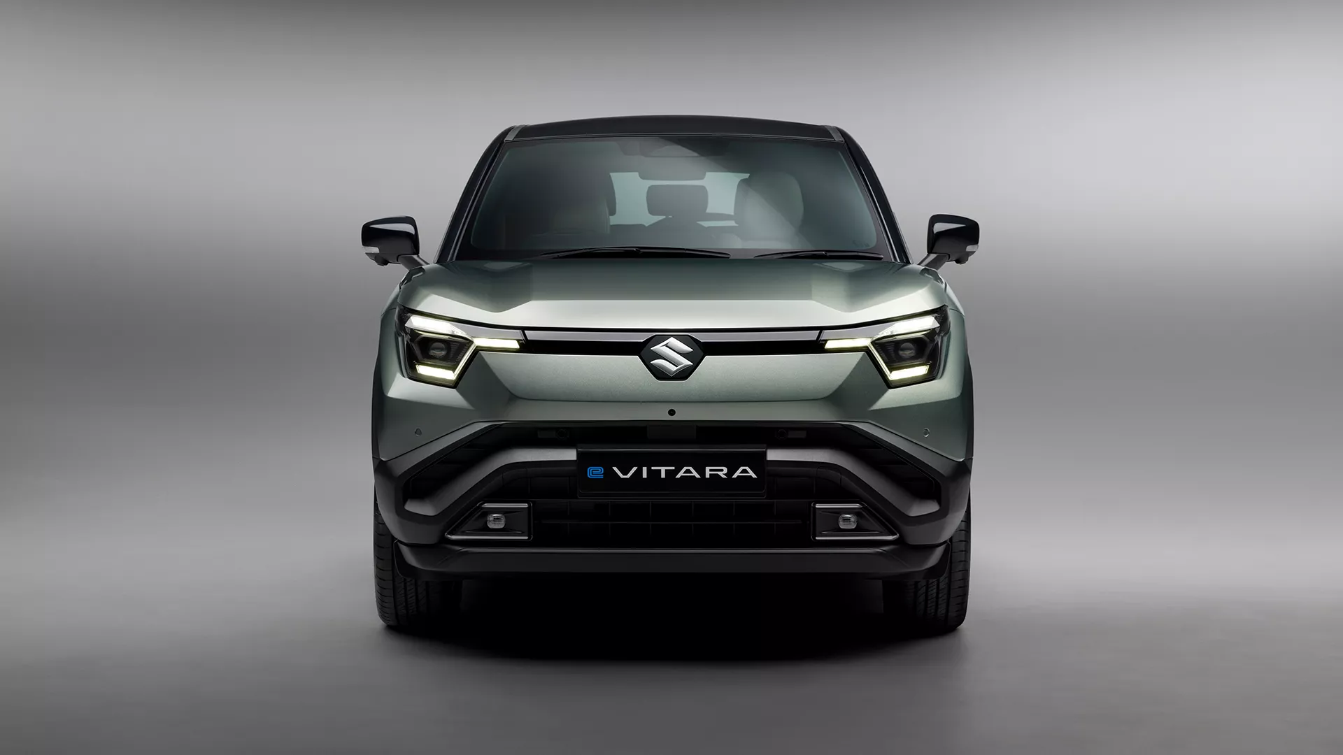 Front view of the Suzuki e Vitara in Land Breeze Green Pearl Metallic, showcasing bold LED headlights and sculpted SUV grille.
