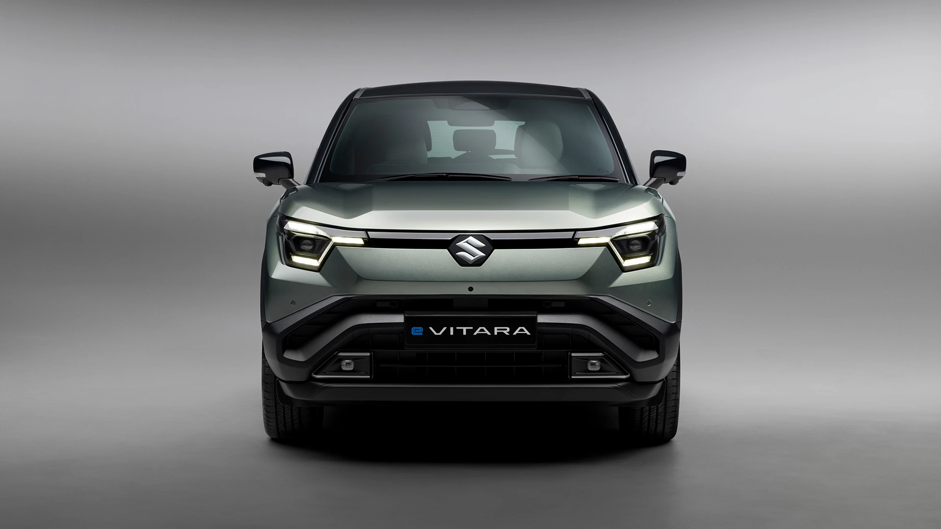 Front view of the Suzuki e Vitara in Land Breeze Green Pearl Metallic, showcasing bold LED headlights and sculpted SUV grille.