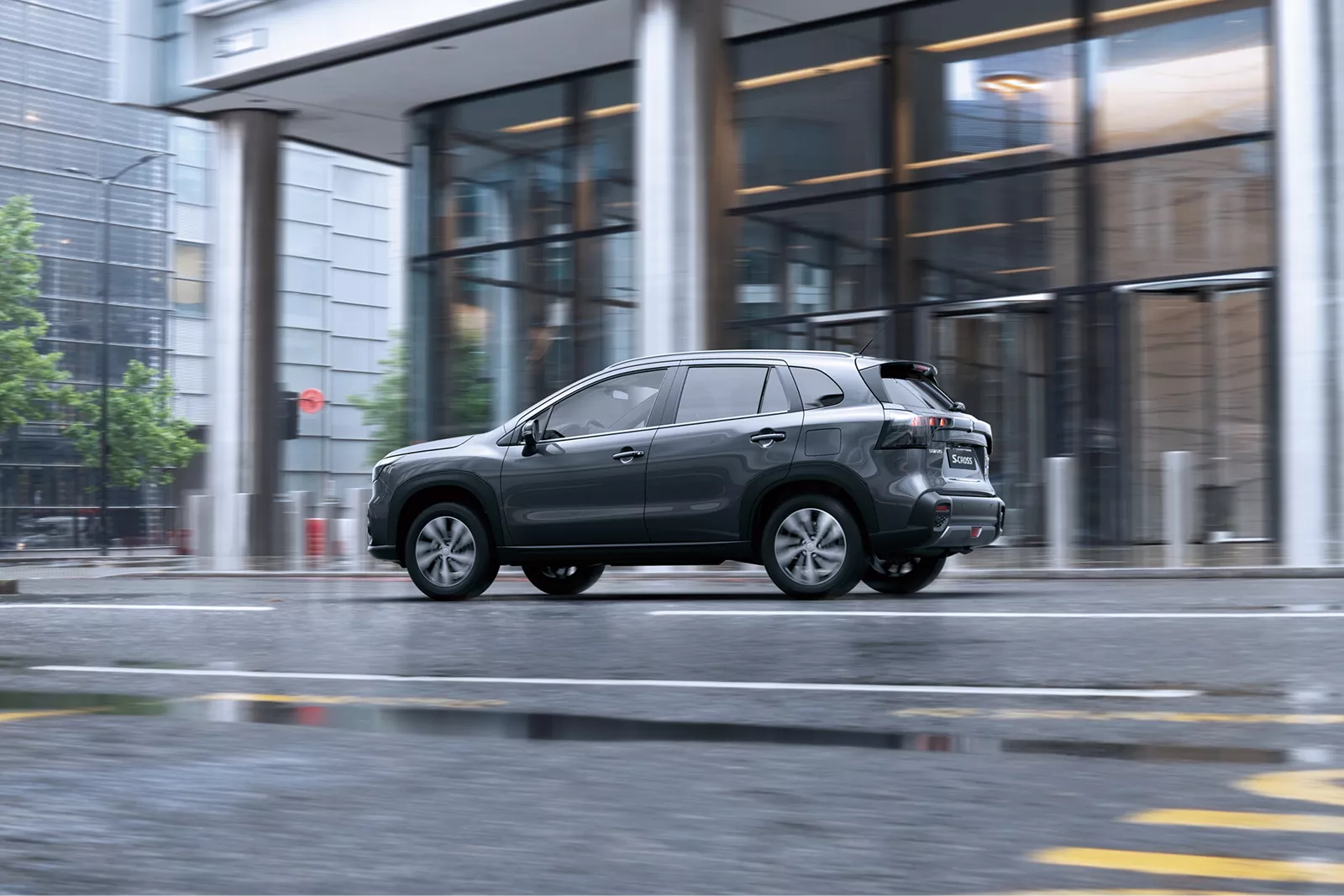 Grey Suzuki S-Cross driving through a modern city street in wet weather