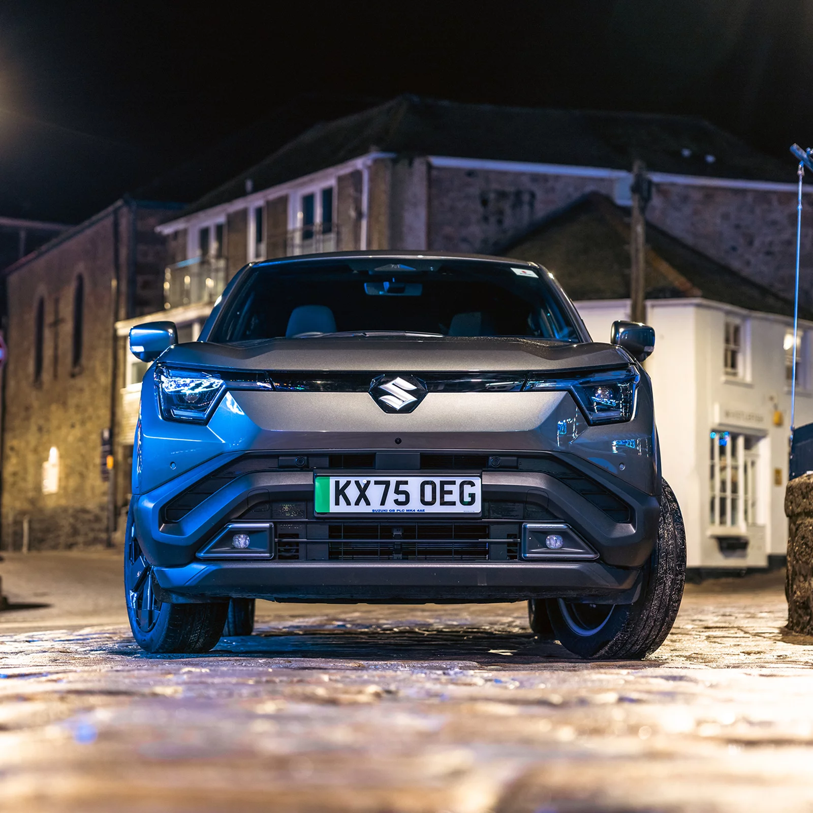 Front view of a Suzuki e Vitara parked on a cobbled street at night