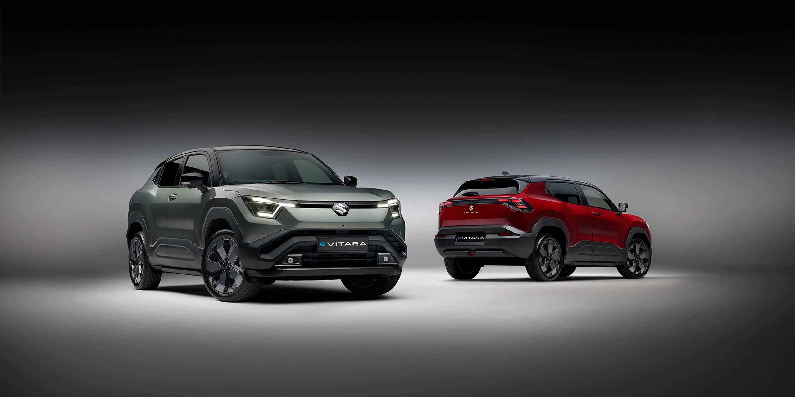 `Front and rear views of grey and red Suzuki e Vitara models on a studio background