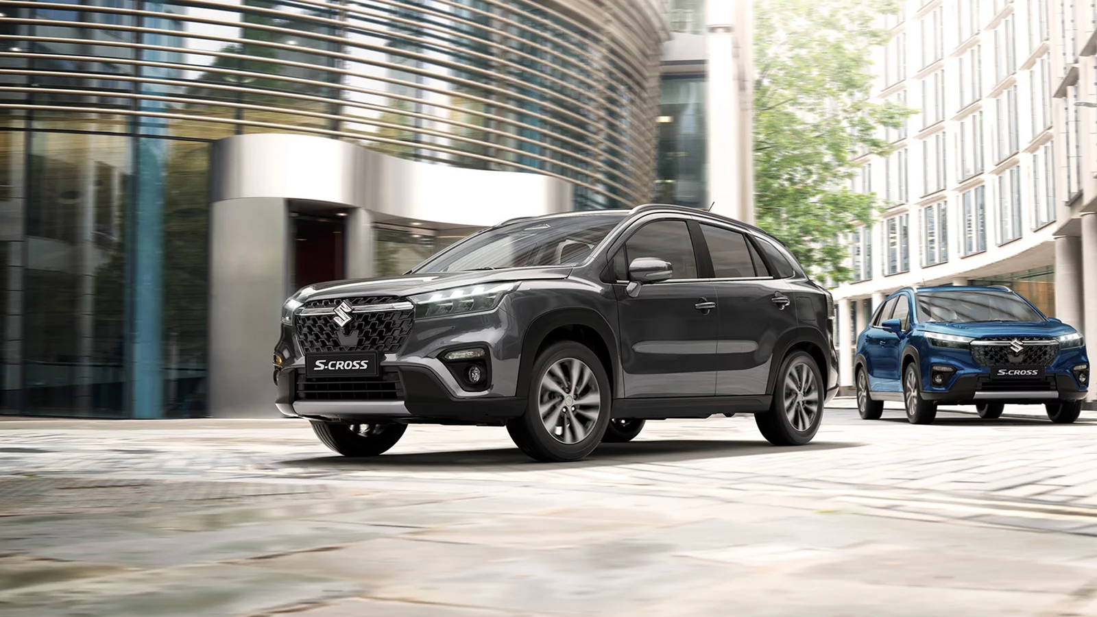 Grey and blue Suzuki S-Cross models driving through a modern city street