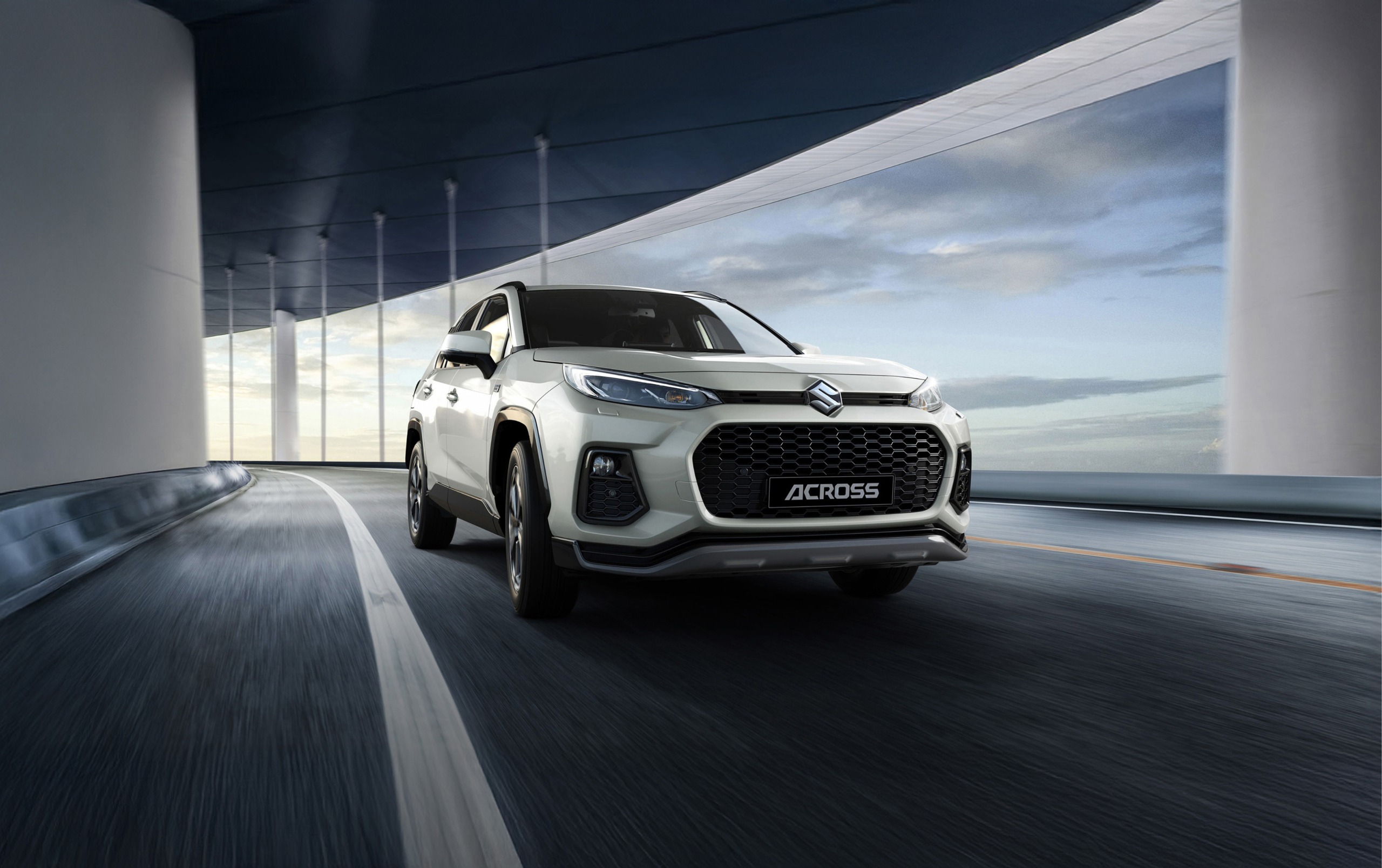 Suzuki Across driving on a curved road, highlighting its bold front grille and dynamic SUV design.