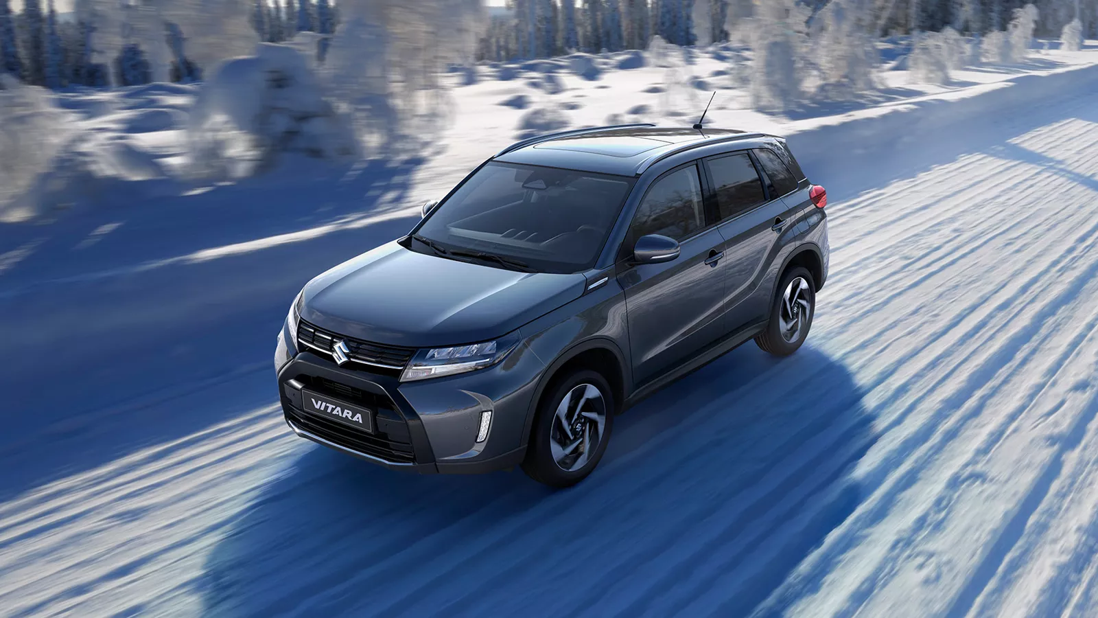 Titan grey Suzuki Vitara driving on a snow-covered road, showcasing its winter handling and all-wheel drive capability.