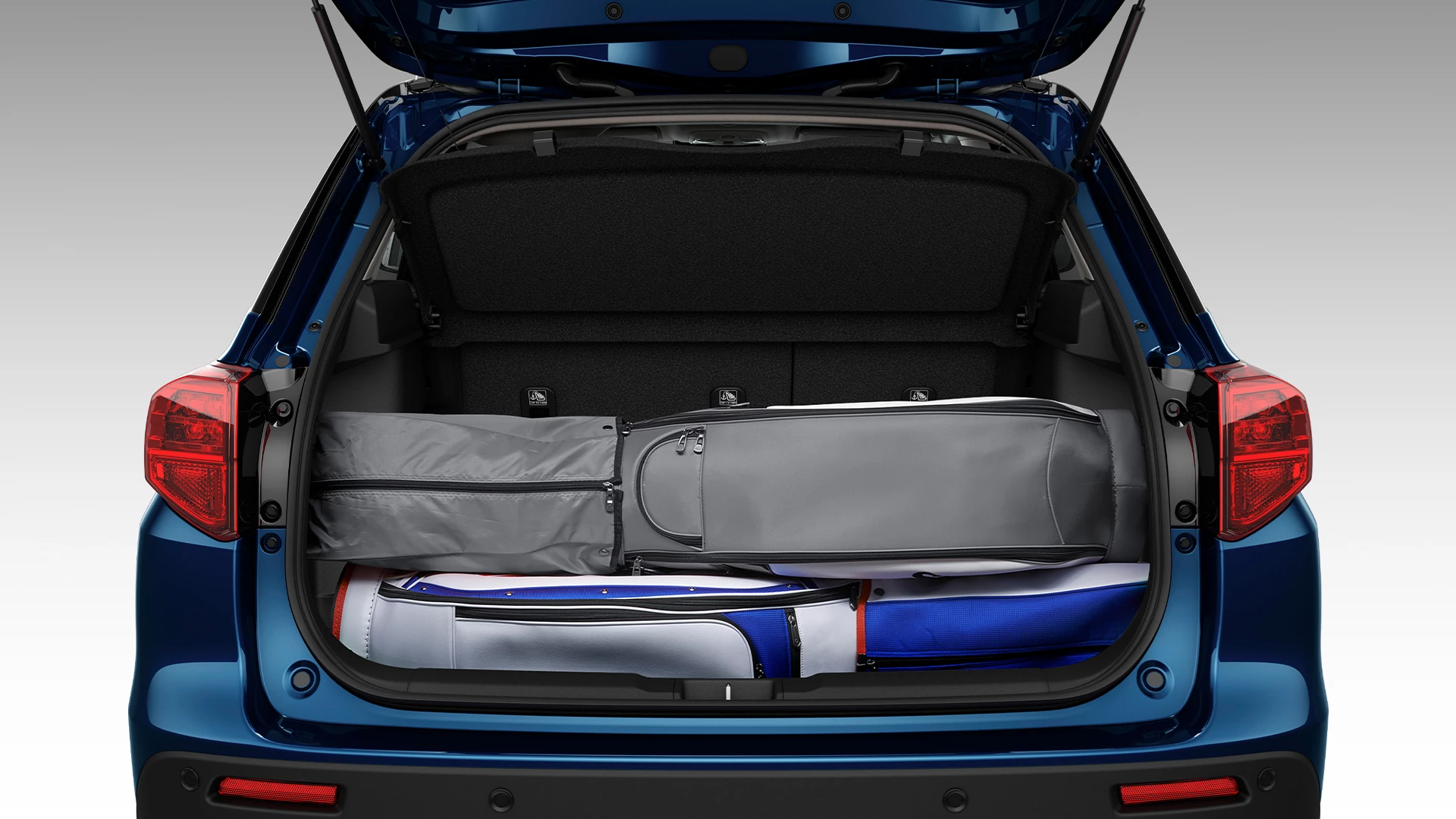 Open boot of the Suzuki Vitara showcasing an adjustable luggage floor with various travel bags neatly stored underneath for flexible storage configuration.