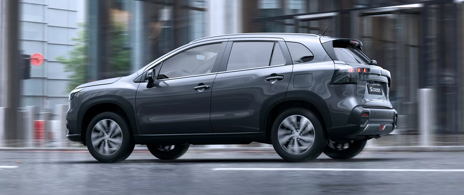Titan grey Suzuki S-Cross driving through a city street in wet conditions, highlighting its sleek design and everyday practicality.