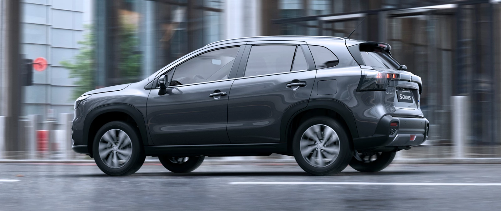 Titan grey Suzuki S-Cross driving through a city street in wet conditions, highlighting its sleek design and everyday practicality.