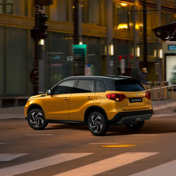 Suzuki Vitara SUV driving through a modern city street at night.
