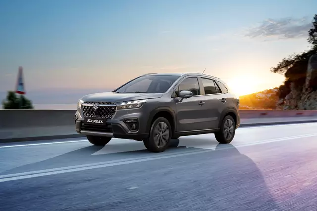 Side view of a grey Suzuki S-Cross on an asphalt road at sunset.