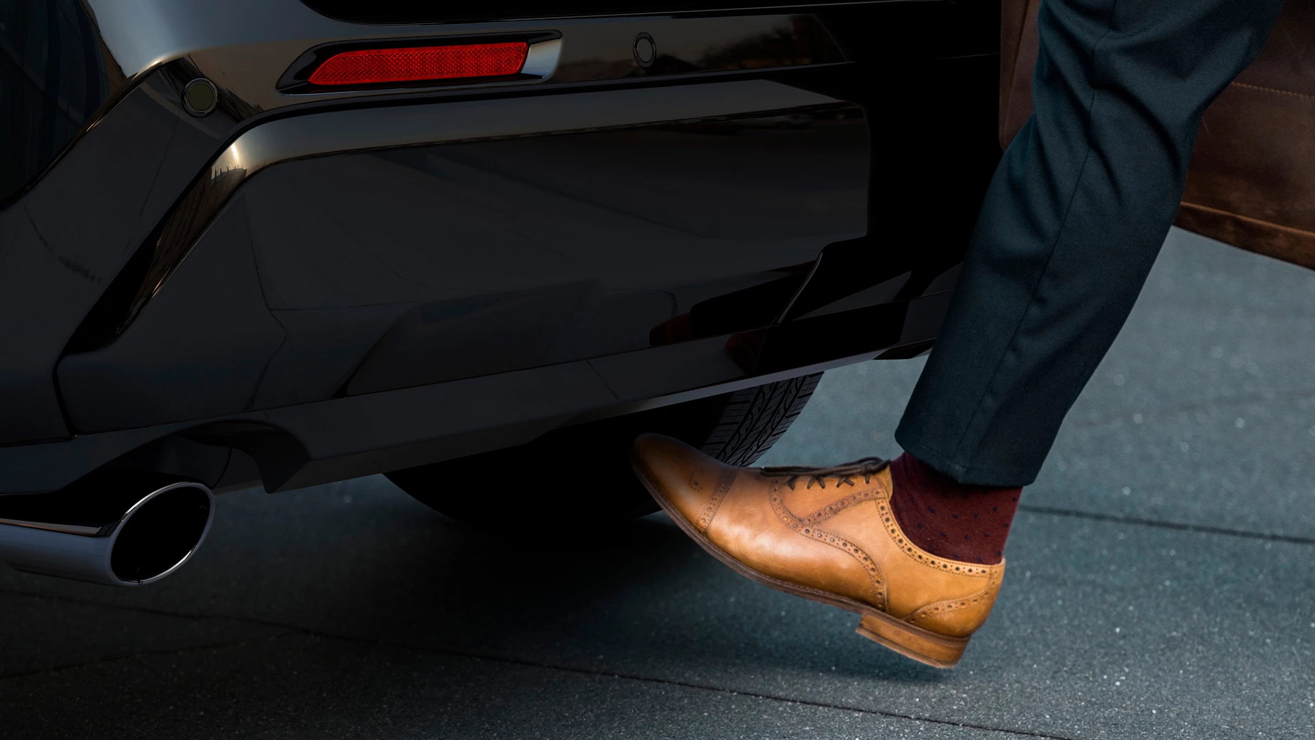 Close-up of a person activating the Suzuki Across kick-operated tailgate by moving their foot beneath the rear bumper, enabling hands-free boot access.