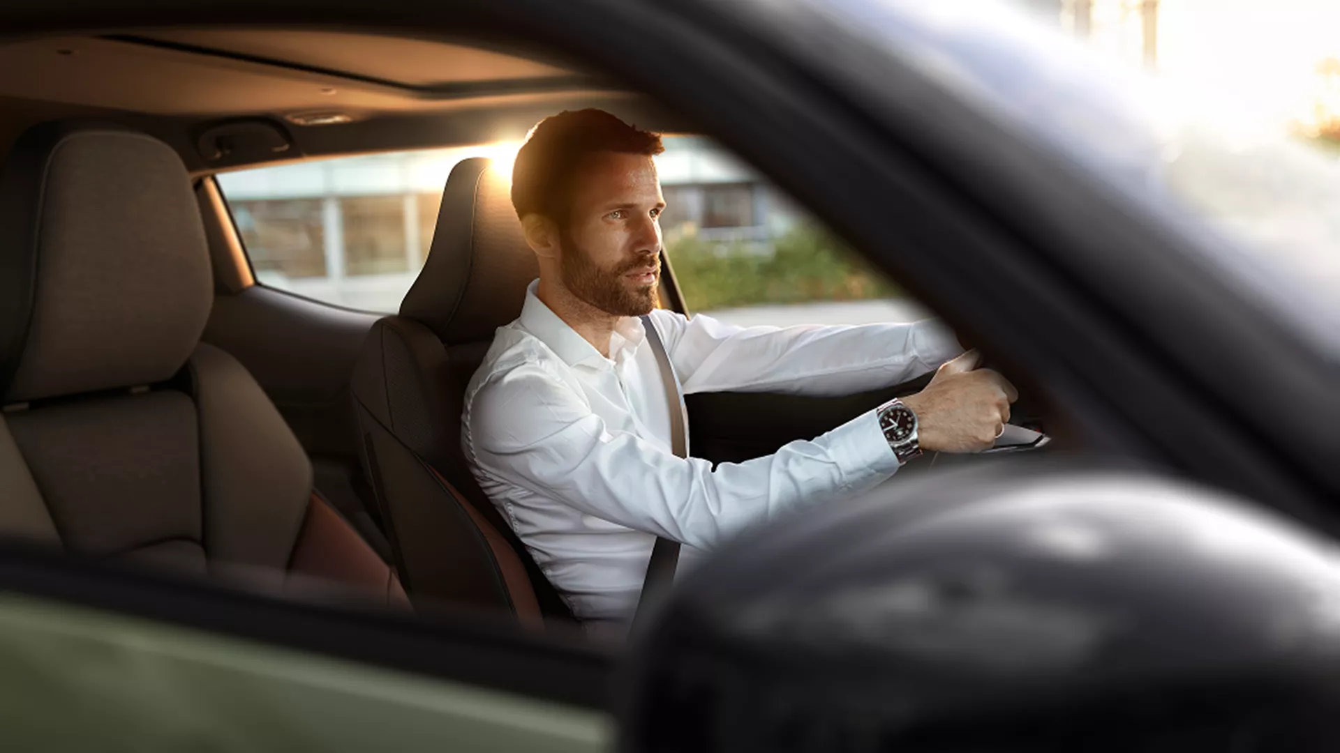 Man driving a car during sunset viewed through the passenger window