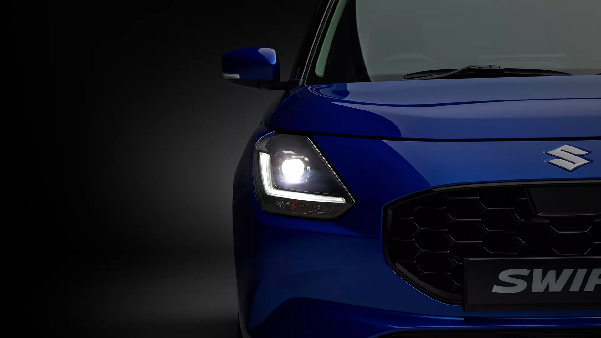 Close-up of the Suzuki Swift front with LED headlight illuminated, showcasing bold styling and vibrant body colour