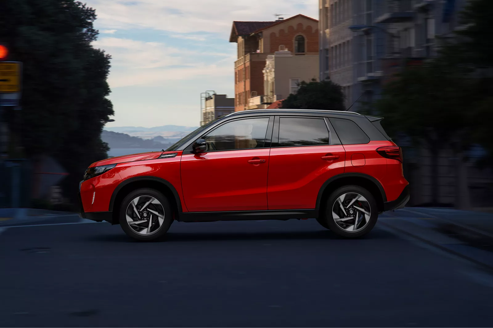 Red Suzuki Vitara driving through a city street at dusk