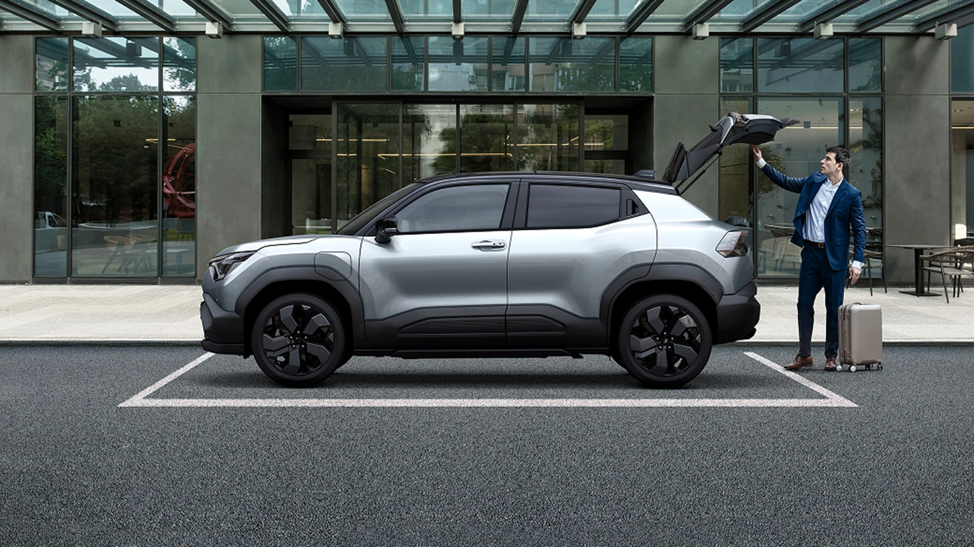 Silver Suzuki e Vitara with the boot open as a driver unloads luggage.