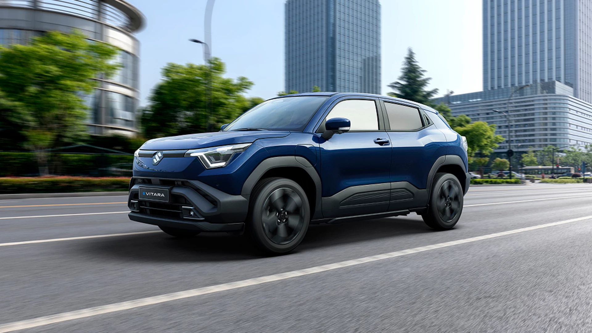 Blue Suzuki e Vitara driving through a modern city.