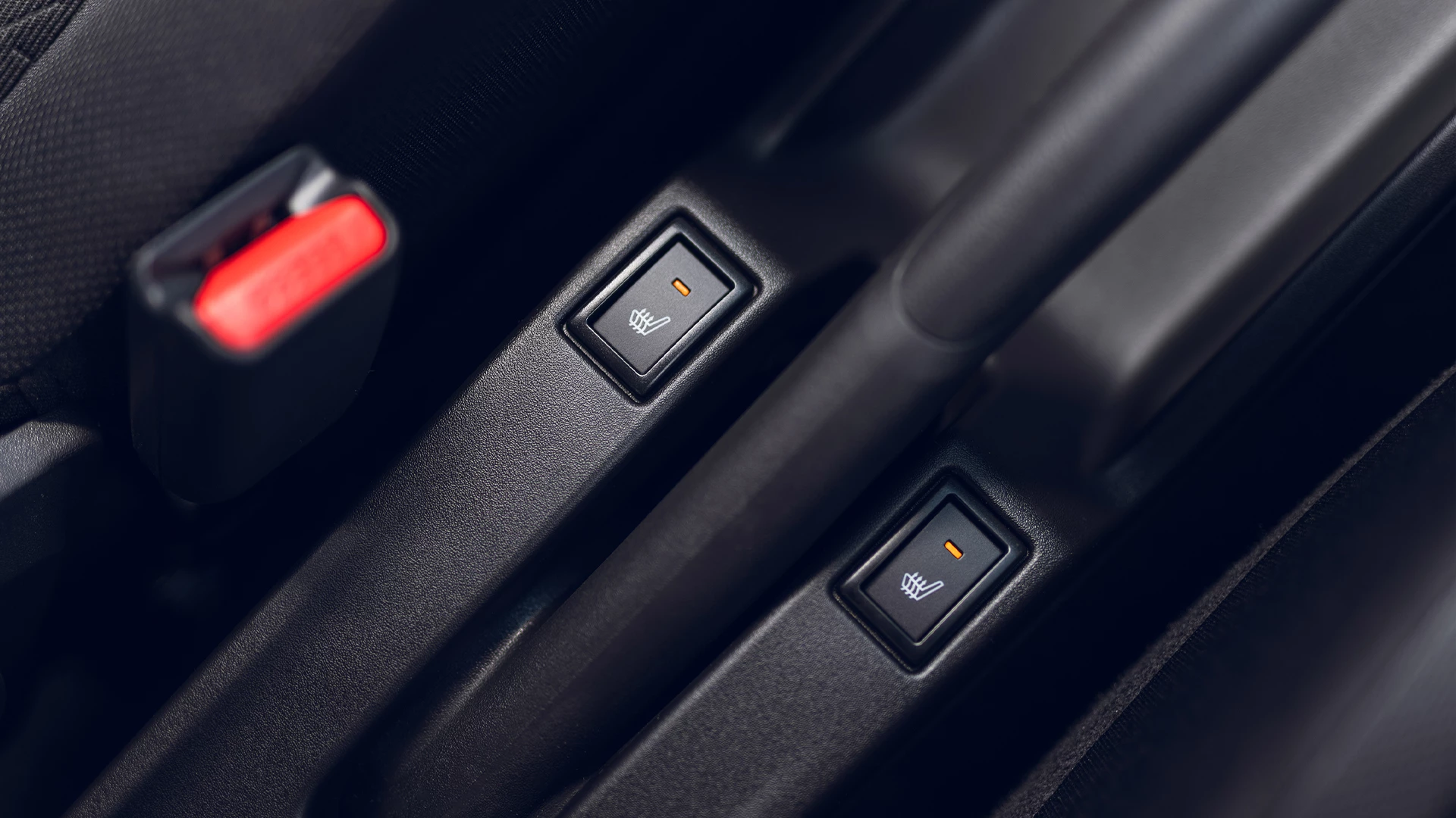 Close-up of Suzuki Swift interior showing illuminated controls for heated front seats beside the handbrake