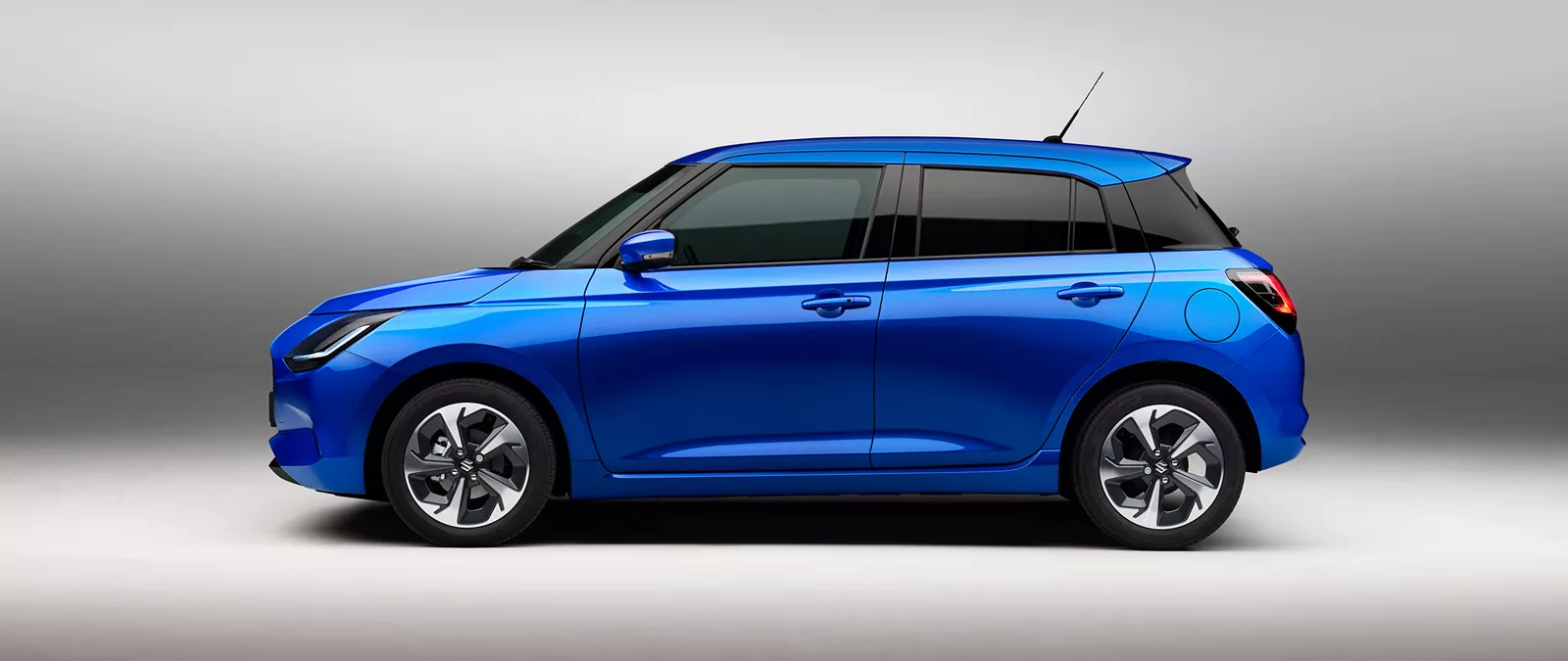 Side view of the Suzuki Swift in frontier blue pearl metallic, highlighting its compact hatchback design and alloy wheels
