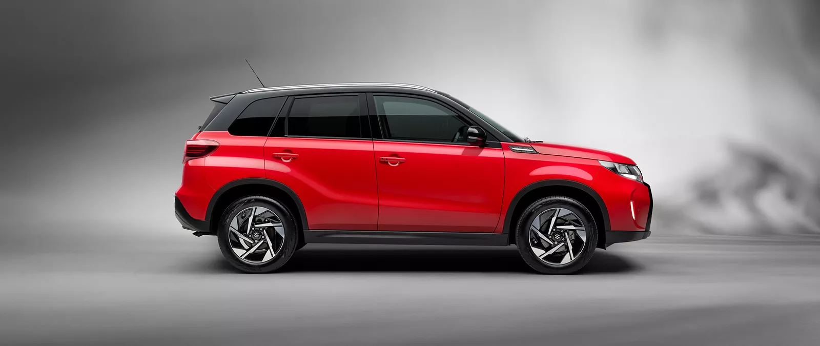 Side view of the Suzuki Vitara in dual tone bright red and cosmic black, displayed in a studio setting against a neutral grey background.