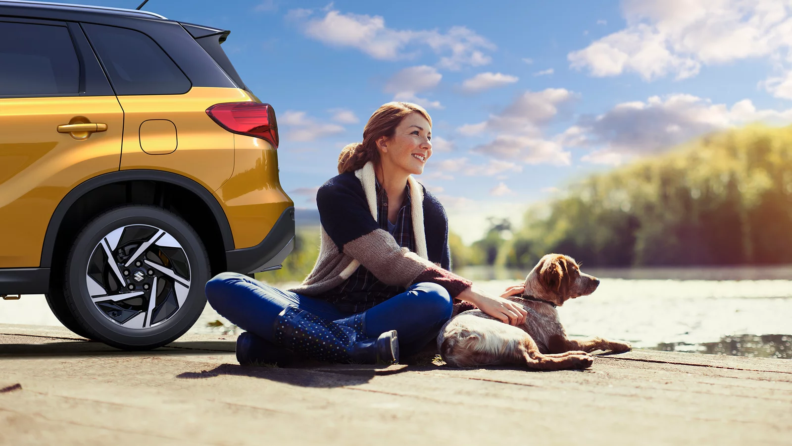 Woman sitting beside a yellow Suzuki SUV with a dog by the water